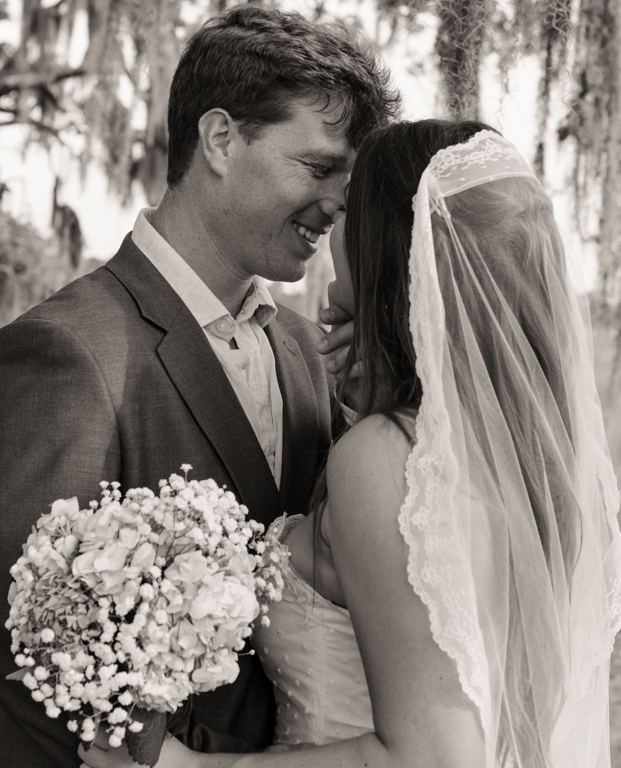 Black and white portrait of bride and groom smiling together, bouquet in foreground. 