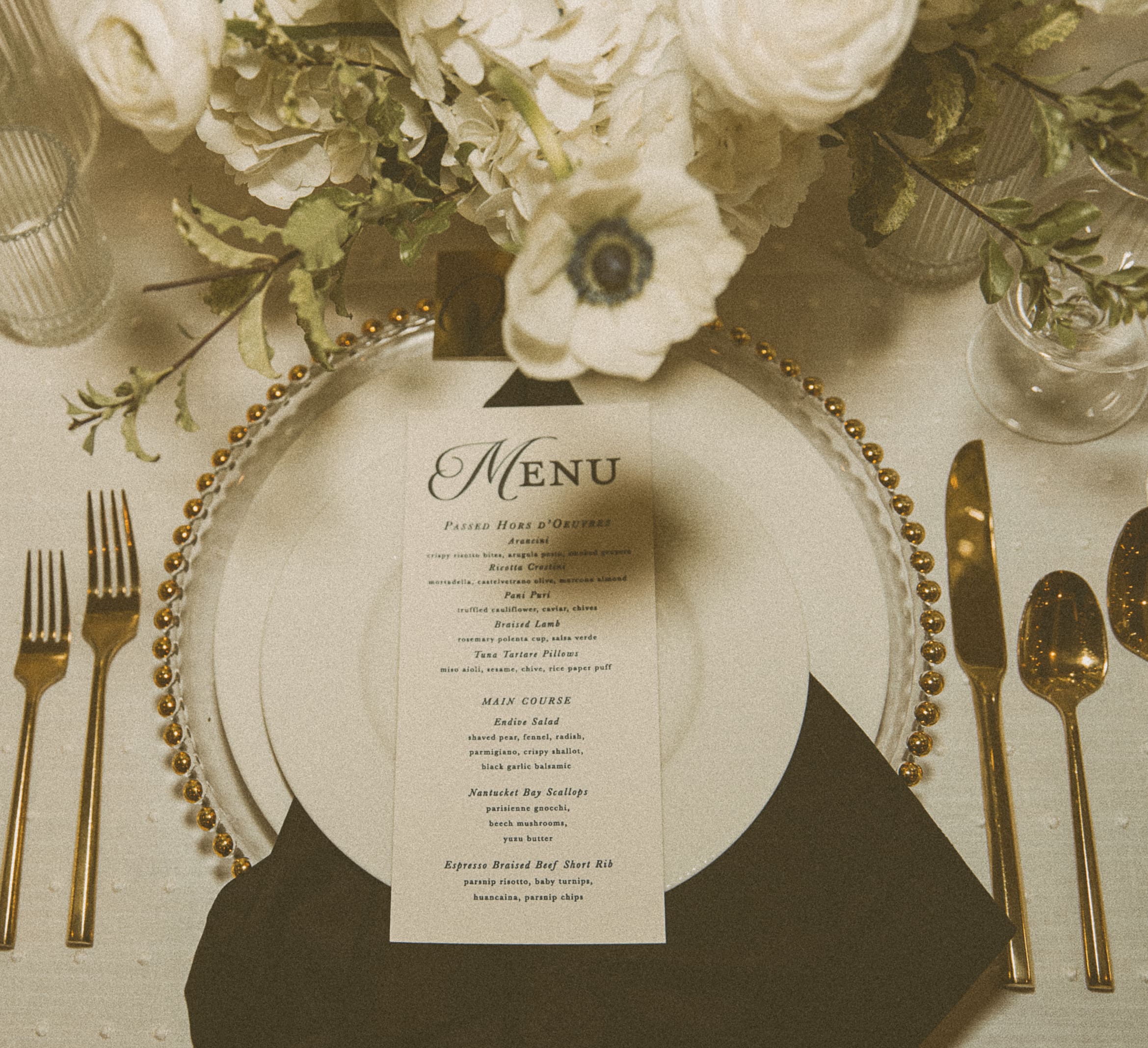 Editorial flatlay of wedding menu and floral accents, styled with golden tones and textured light to capture elevated reception details. 