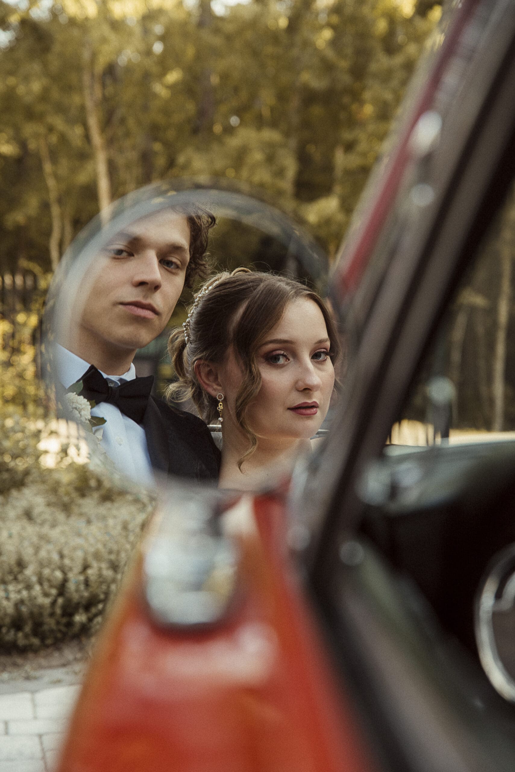 Editorial portrait of bride and groom at sunset in mirror of 1967 classic red mustang. Captured by wedding photographer Brandi Denslow.