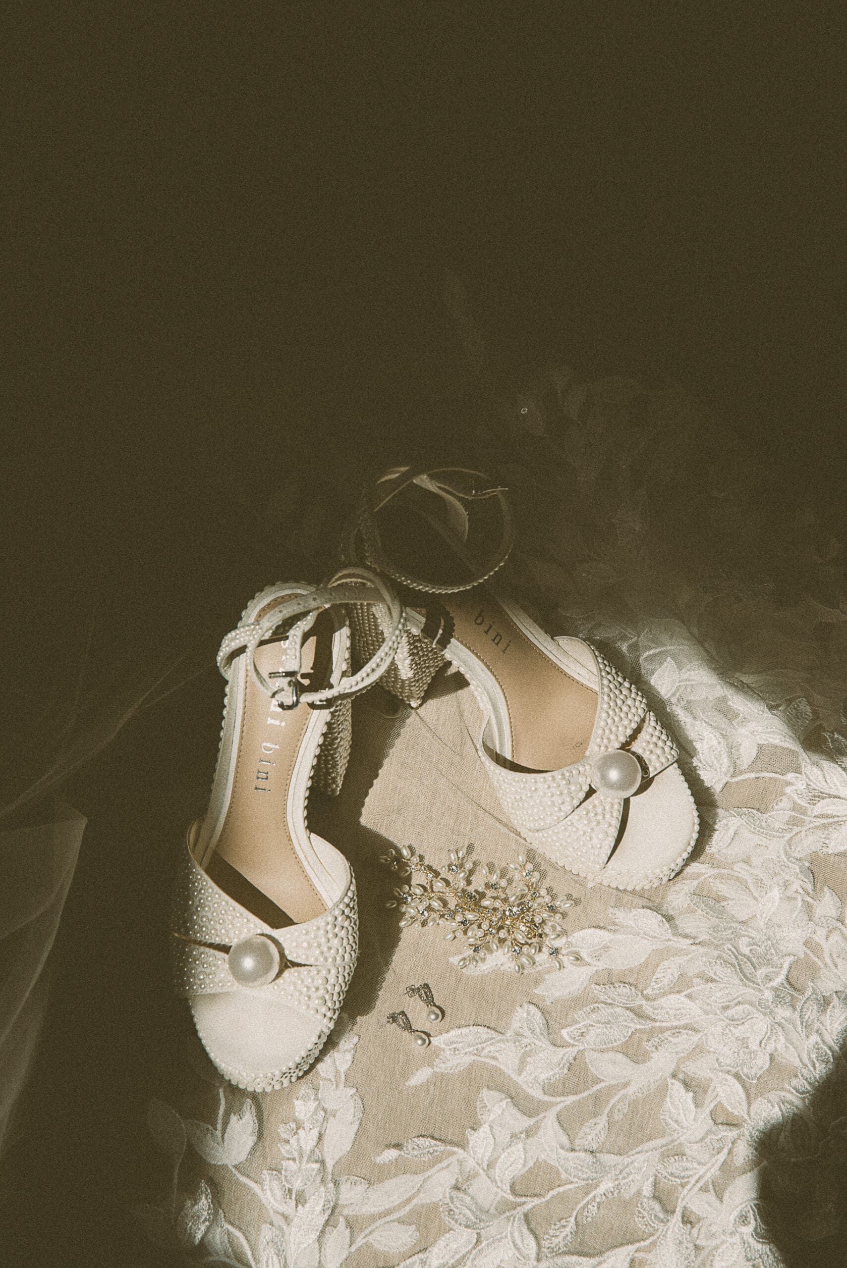 Editorial detail photo of pearl-adorned bridal heels and jewelry styled on lace, showcasing the quiet elegance of wedding day storytelling. 