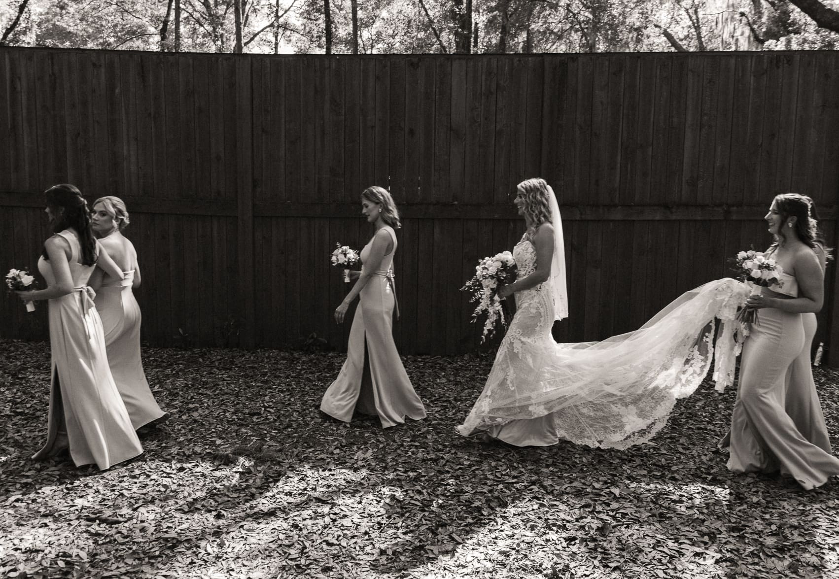 Bride and bridesmaids walking through filtered sunlight beneath tall tress during a St. Augustine wedding ceremony.