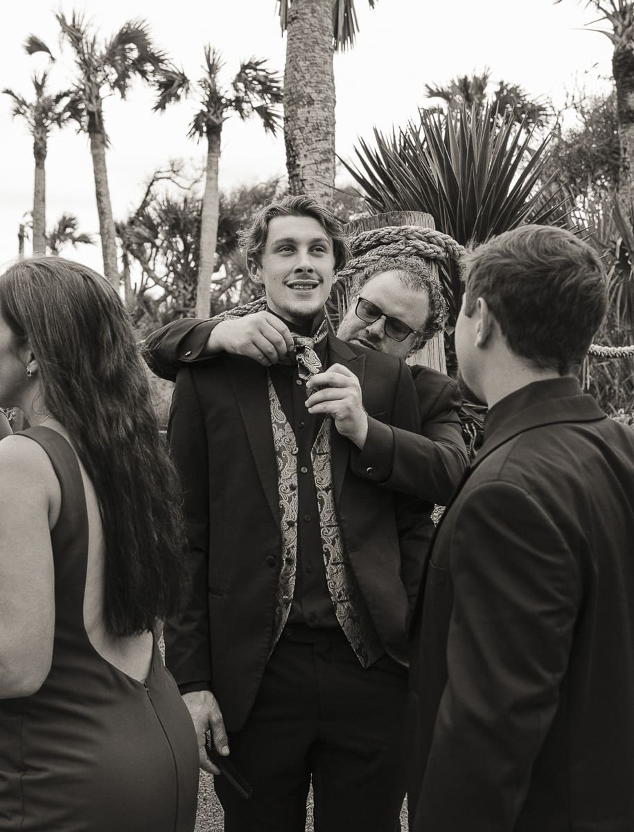 Groom surrounded by wedding party getting tie adjusted before ceremony in Jacksonville, Florida.