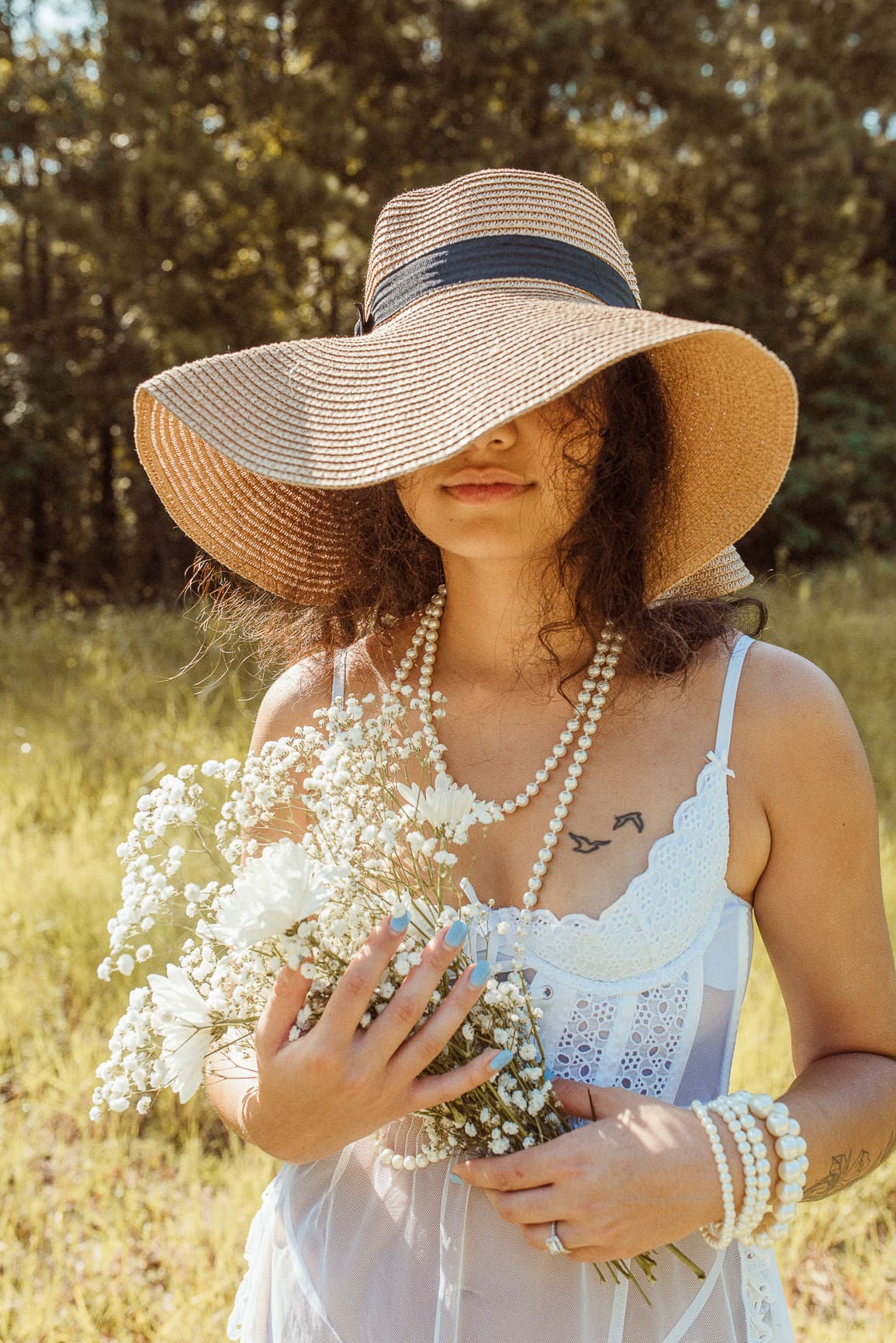 Editorial bridal portrait featuring a bride in a wide brim hat holding delicate florals, photographed with natural light and an unhurried wedding timeline.