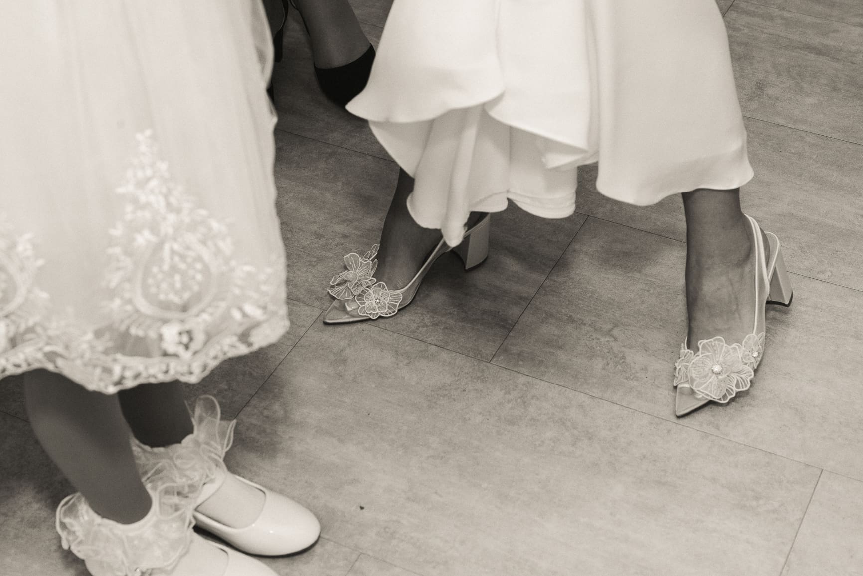 Editorial close-up of bride's embellished heels beneath her gown, highlighting refined style and thoughtful wedding day details. 