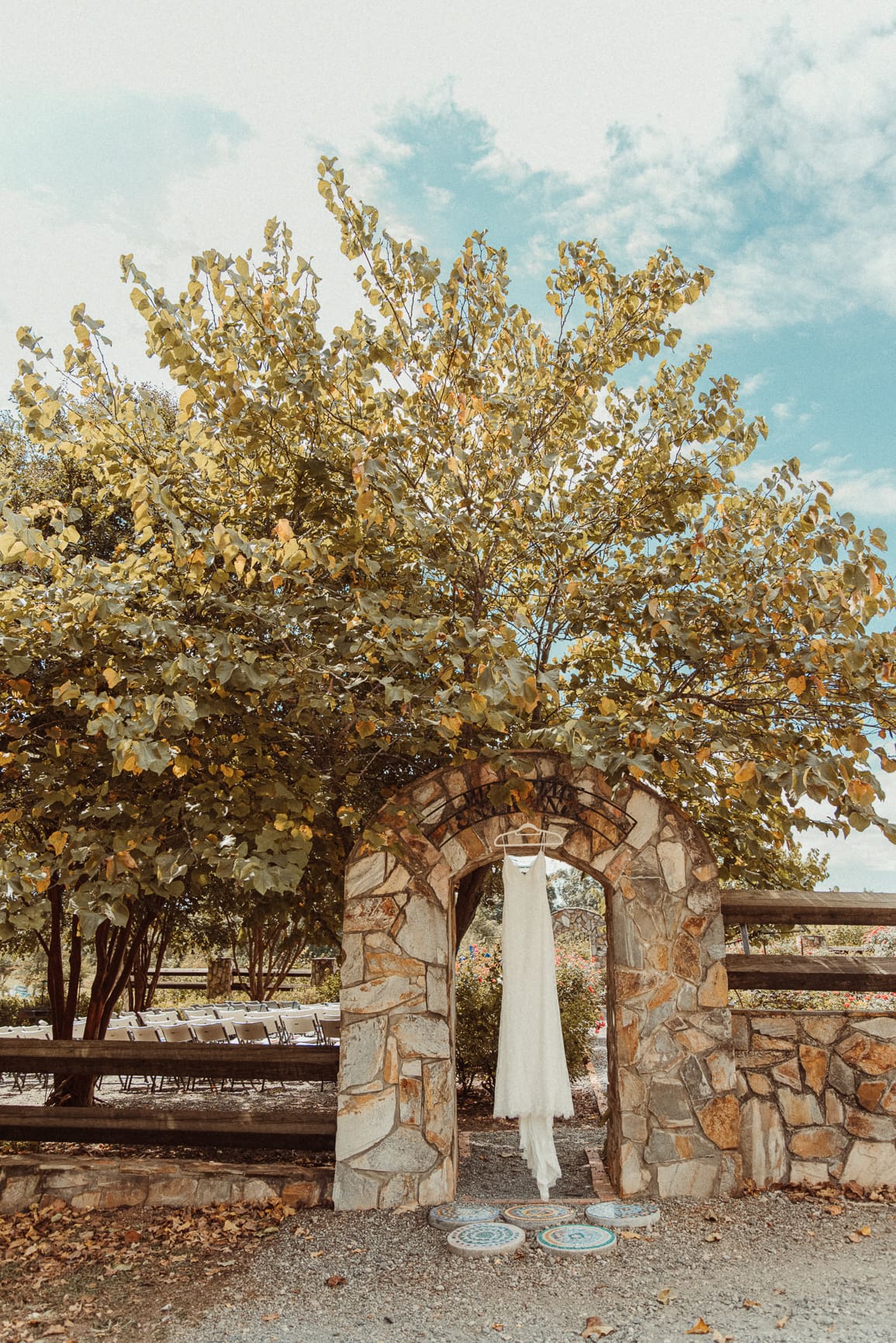 Bridal gown displayed beneath a stone archway surrounded by trees, photographed in natural light for an editorial yet organic feel. 