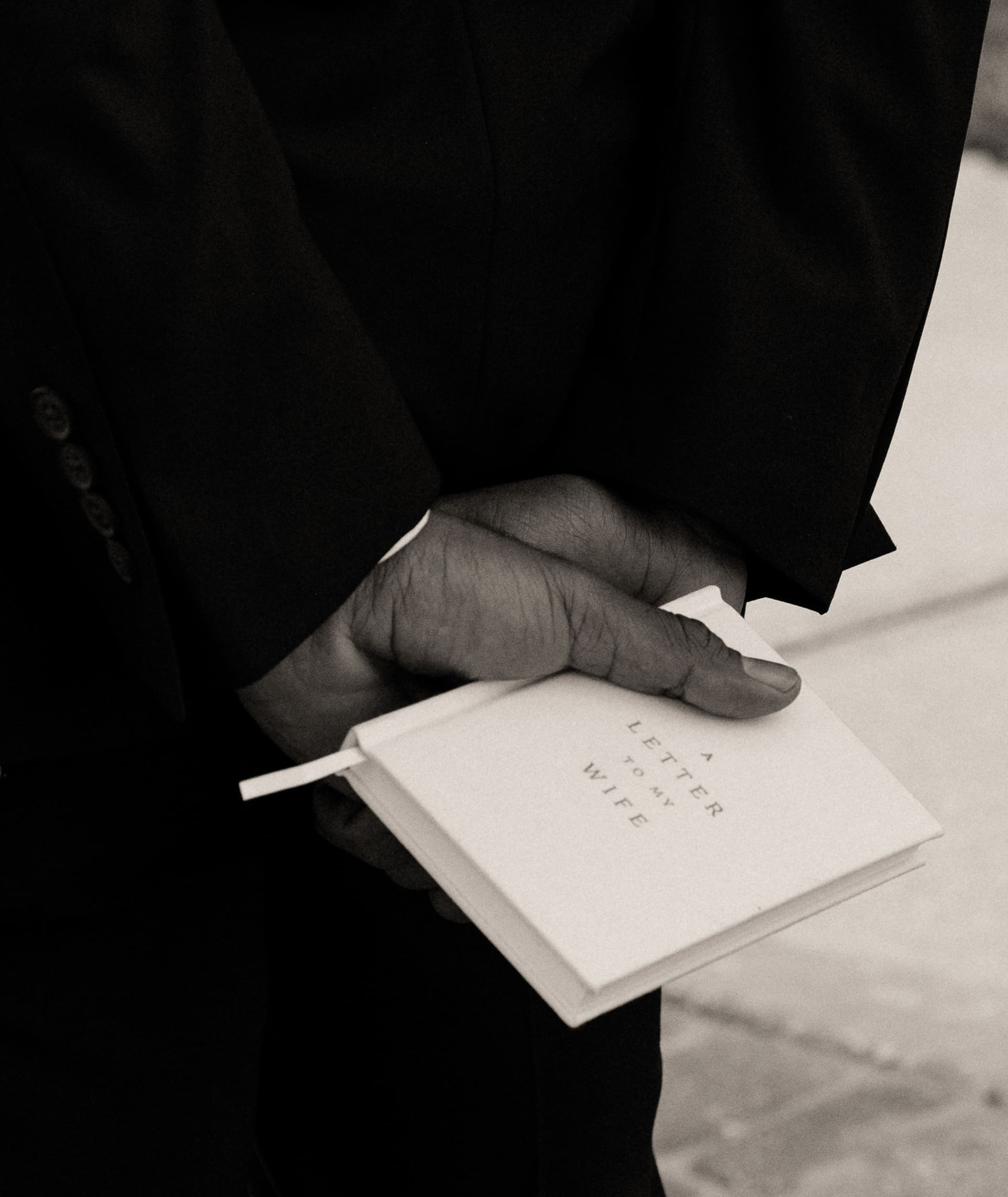 Black and white detail of a groom's hand holding a "Letter to My Wife" book before the ceremony.