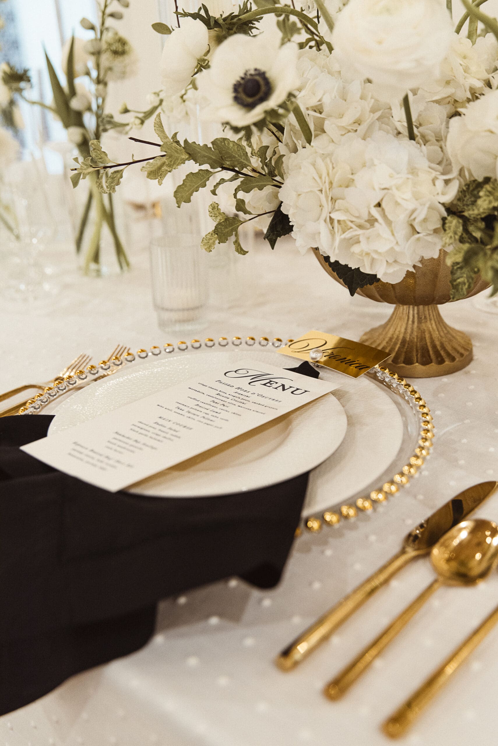 Gold flatware and menu card detail on a black, white, and gold wedding tablescape