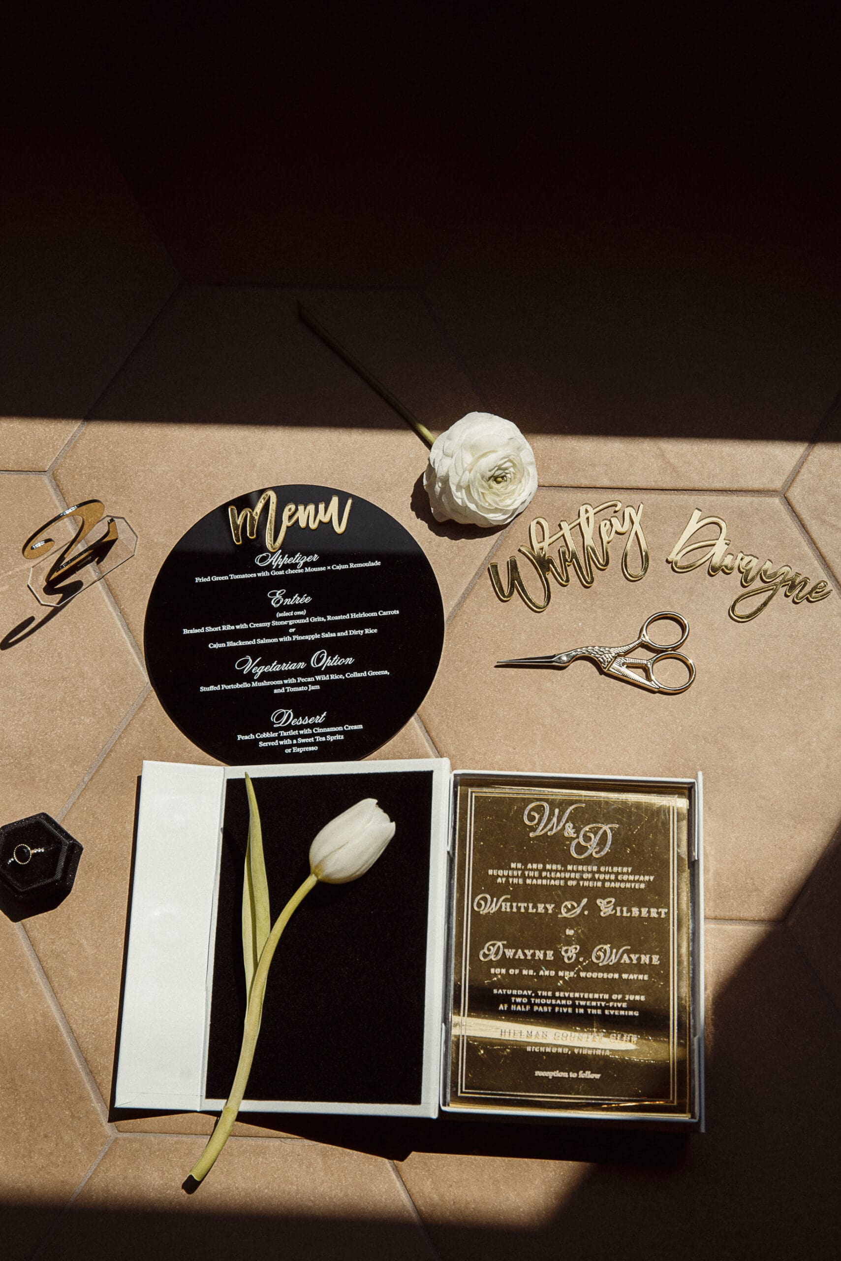 Black and gold wedding stationery suite flat lay, featuring menu card and calligraphy place setting