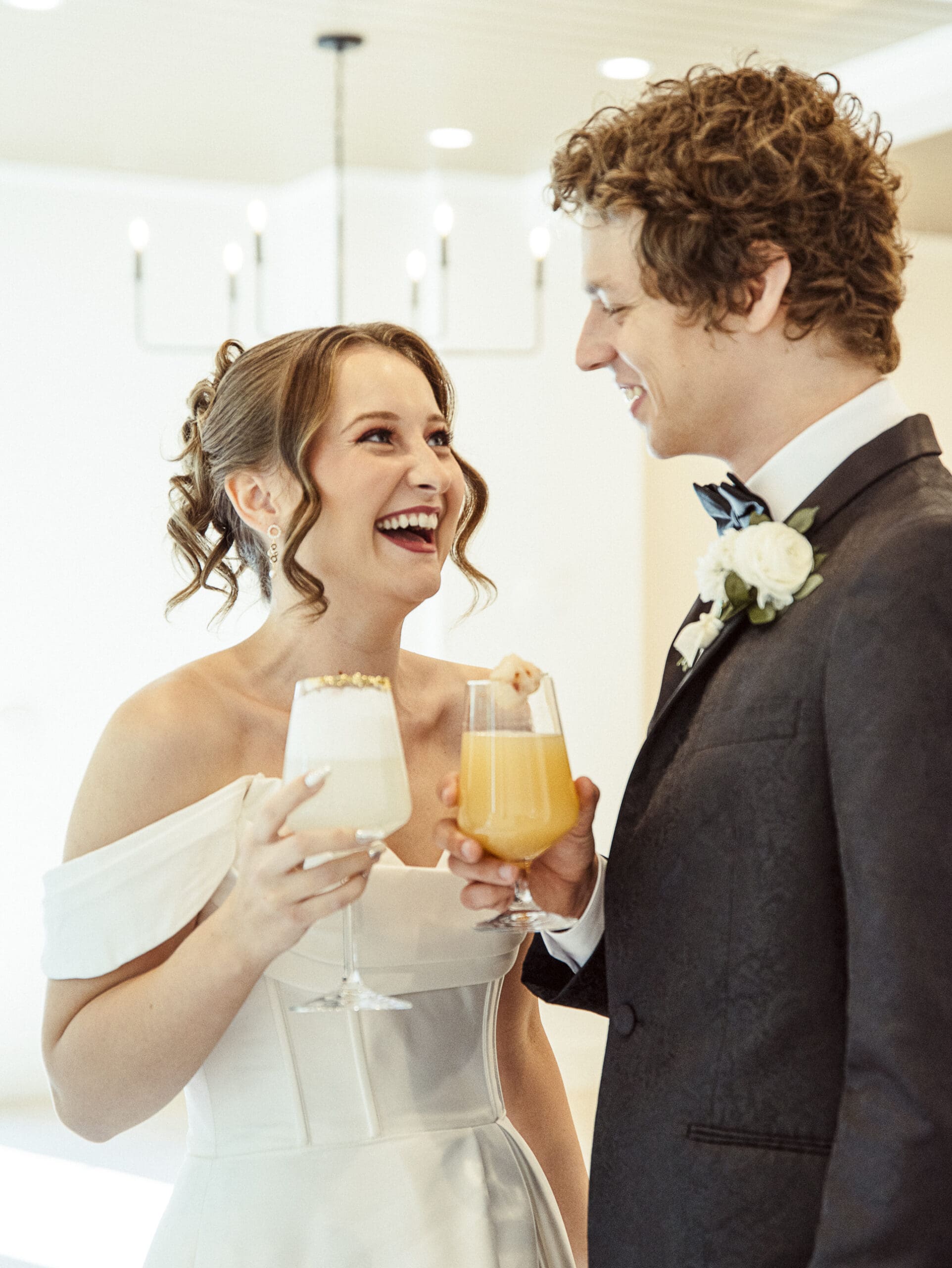 Bride and groom laughing and toasting drinks together during the reception