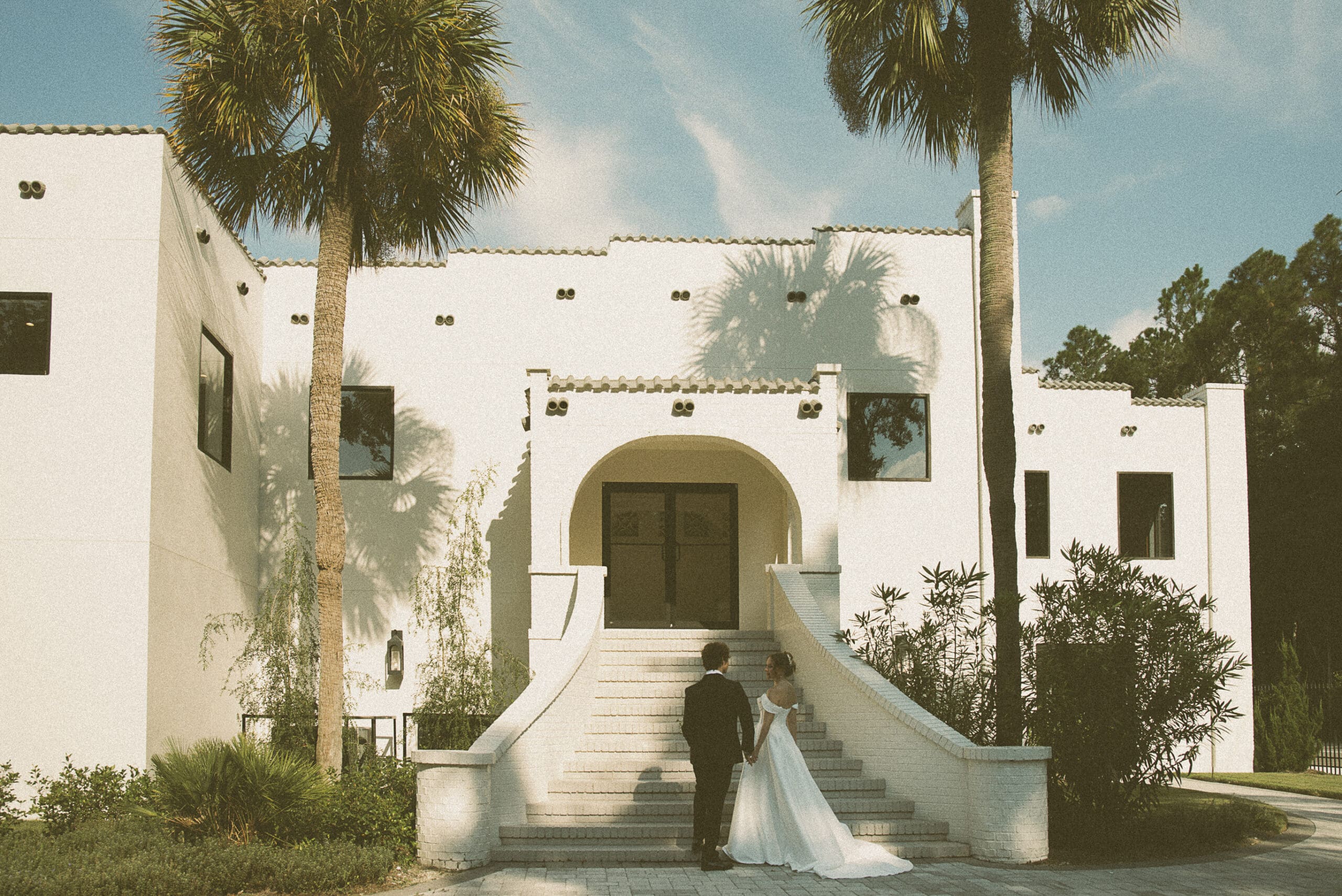 Bride and groom holding hands on the grand staircase of the Old Spanish Quarter, surrounded by palm trees and timeless Spanish architecture.