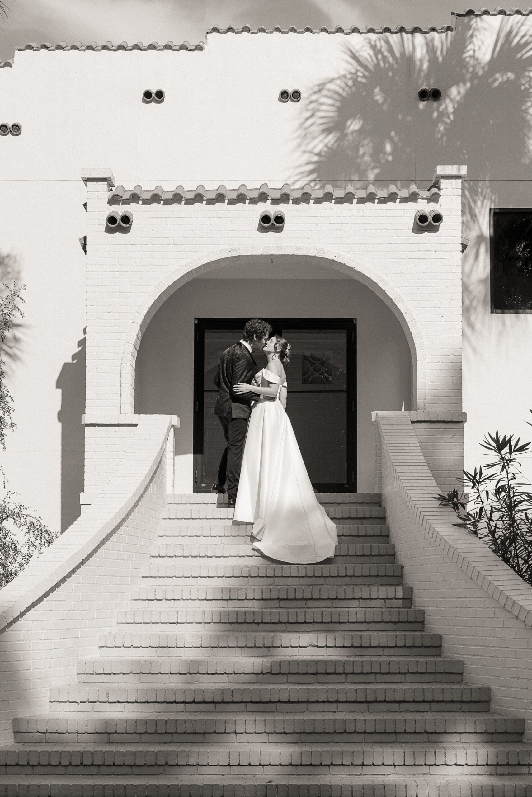 Black-and-white photo of the couple kissing beneath the arched entry atop the grand staircase