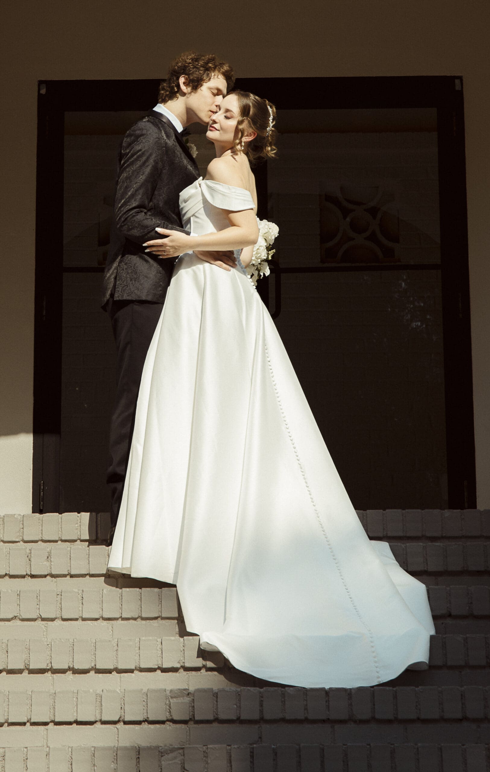Close-up of the bride and groom sharing a kiss on the staircase, golden evening light