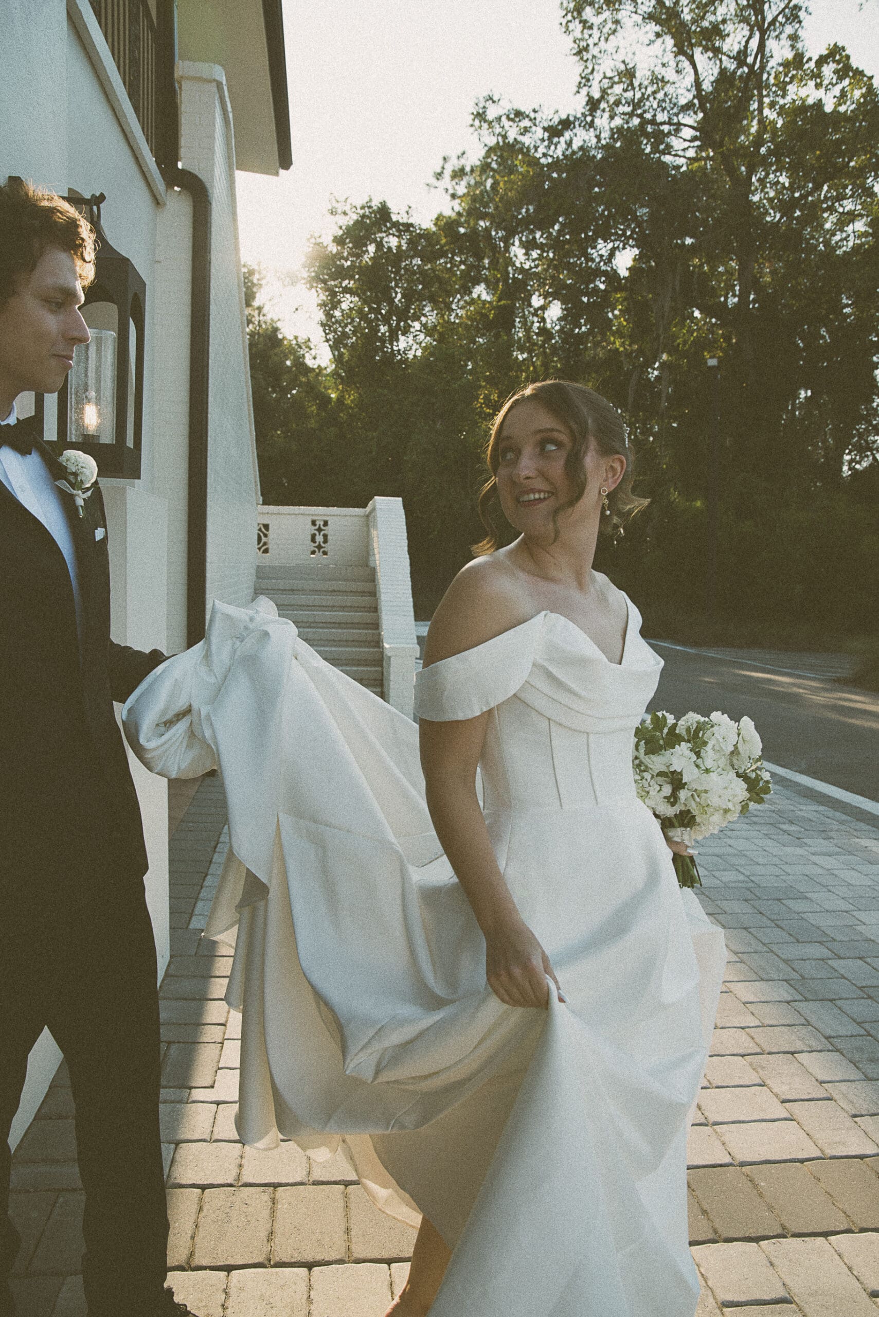 Bride walking down an outdoor pathway at golden hour, bouquet in hand