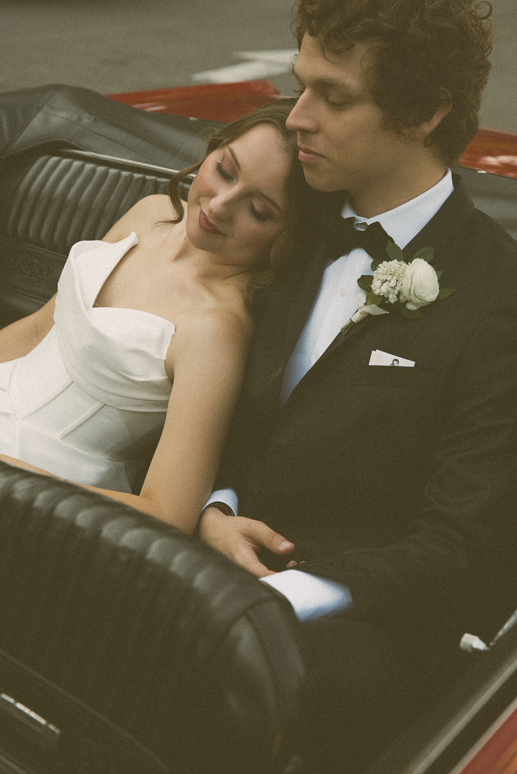 Bride and groom cheek to cheek in the back seat of a vintage car