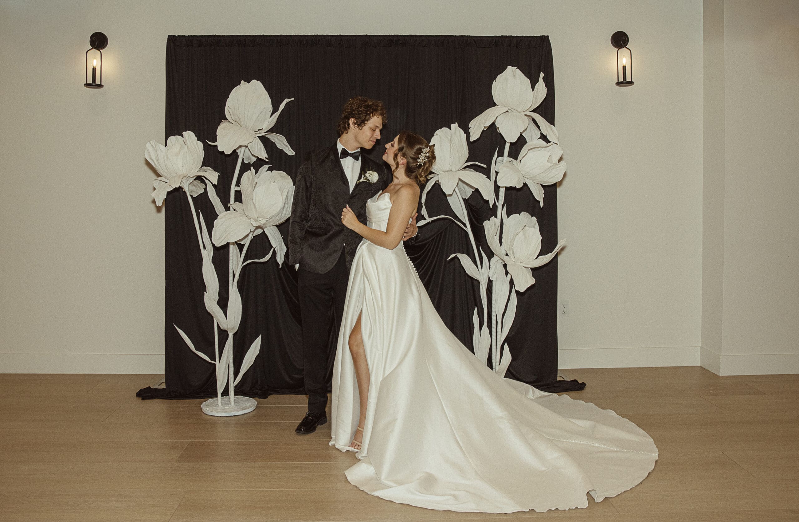Playful editorial wedding portrait at the Old Spanish Quarter featuring a black backdrop with oversized white paper flowers for a modern, artful twist.