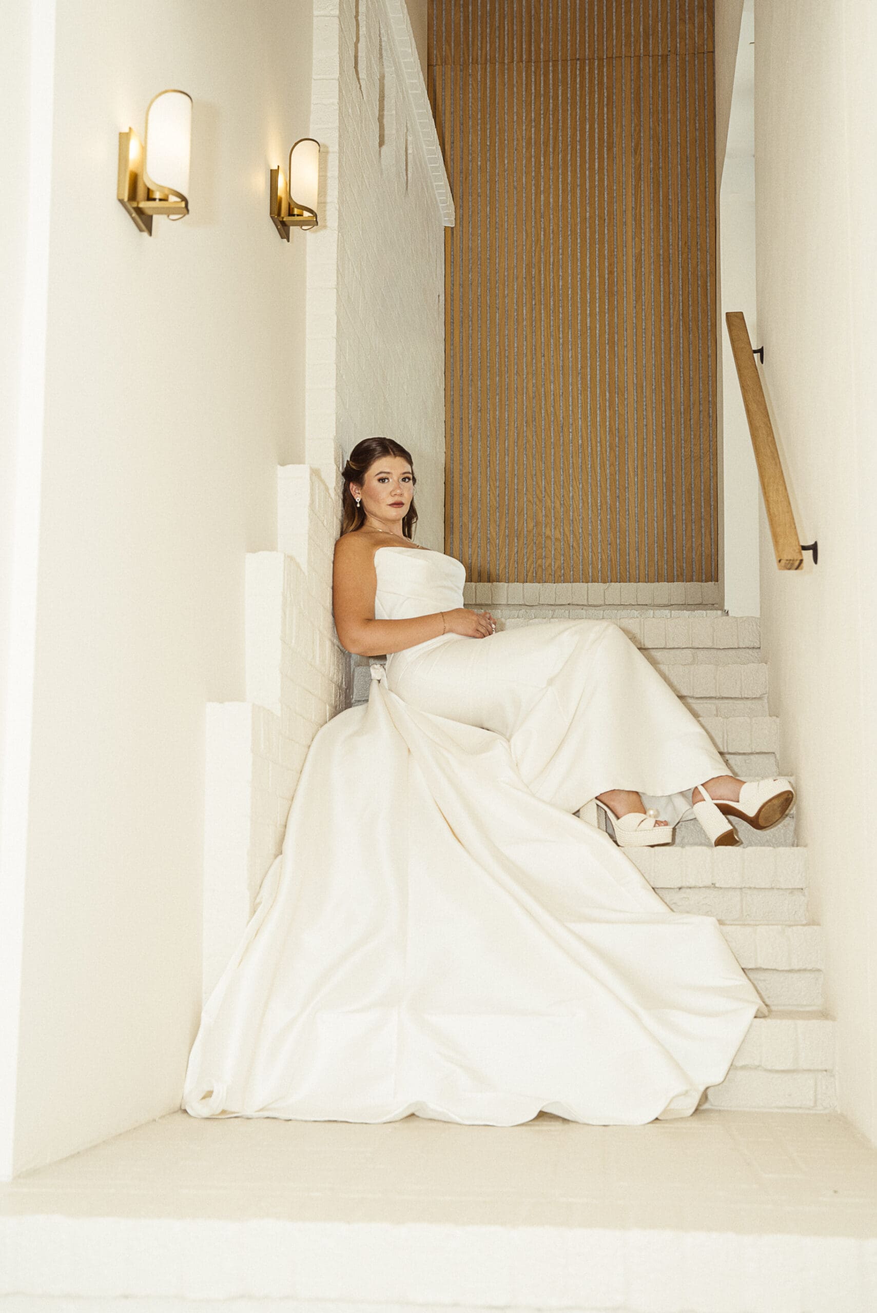 Bride seated on the staircase with her wedding gown train and shoes in view