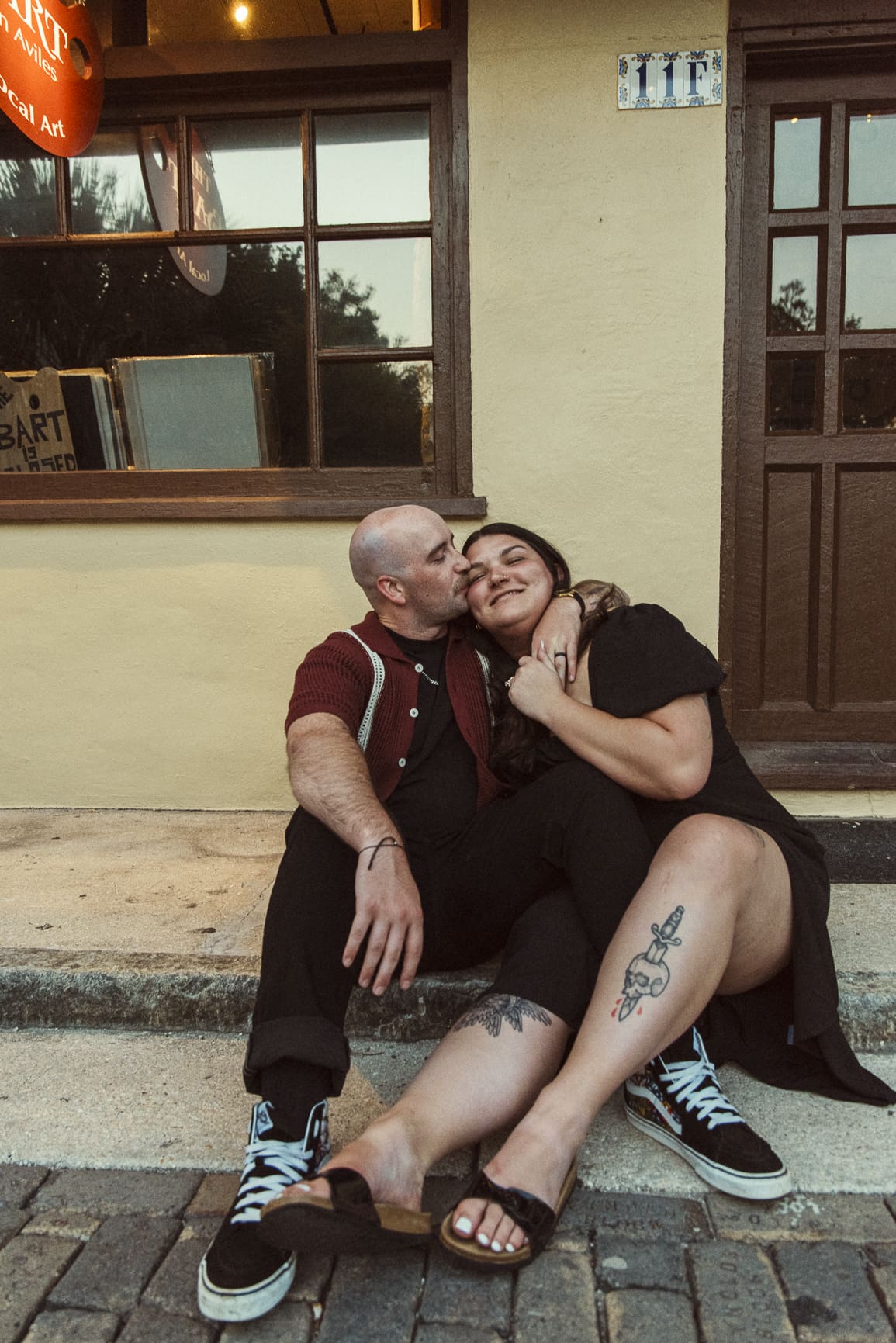 Candid engagement photo of Rebecca and Noah sitting close together on stone steps in downtown St. Augustine, sharing a relaxed and intimate moment. 