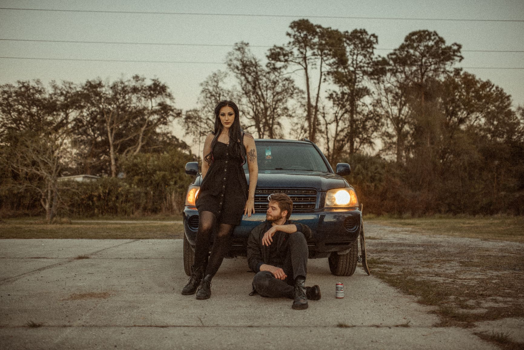 Urban editorial engagement photo of a couple styled in dark fashion and photographed in a parking garage, illustrating how creatively directed engagement sessions turn unexpected locations into art. 