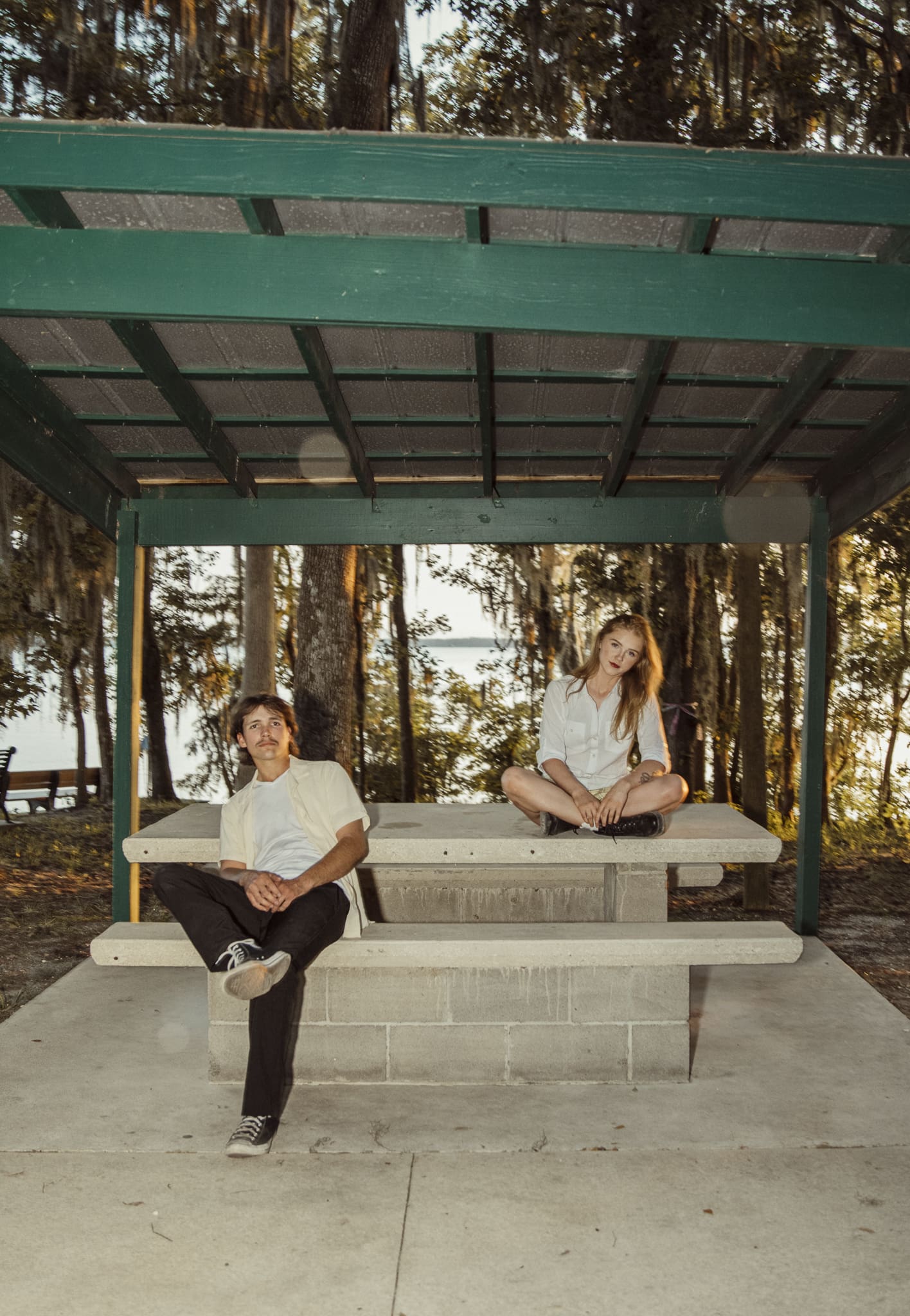 Couple photographed in a creatively directed engagement session with editorial posing and intentional distance, captured under a pavilion for an artistic, non-traditional engagement photo.