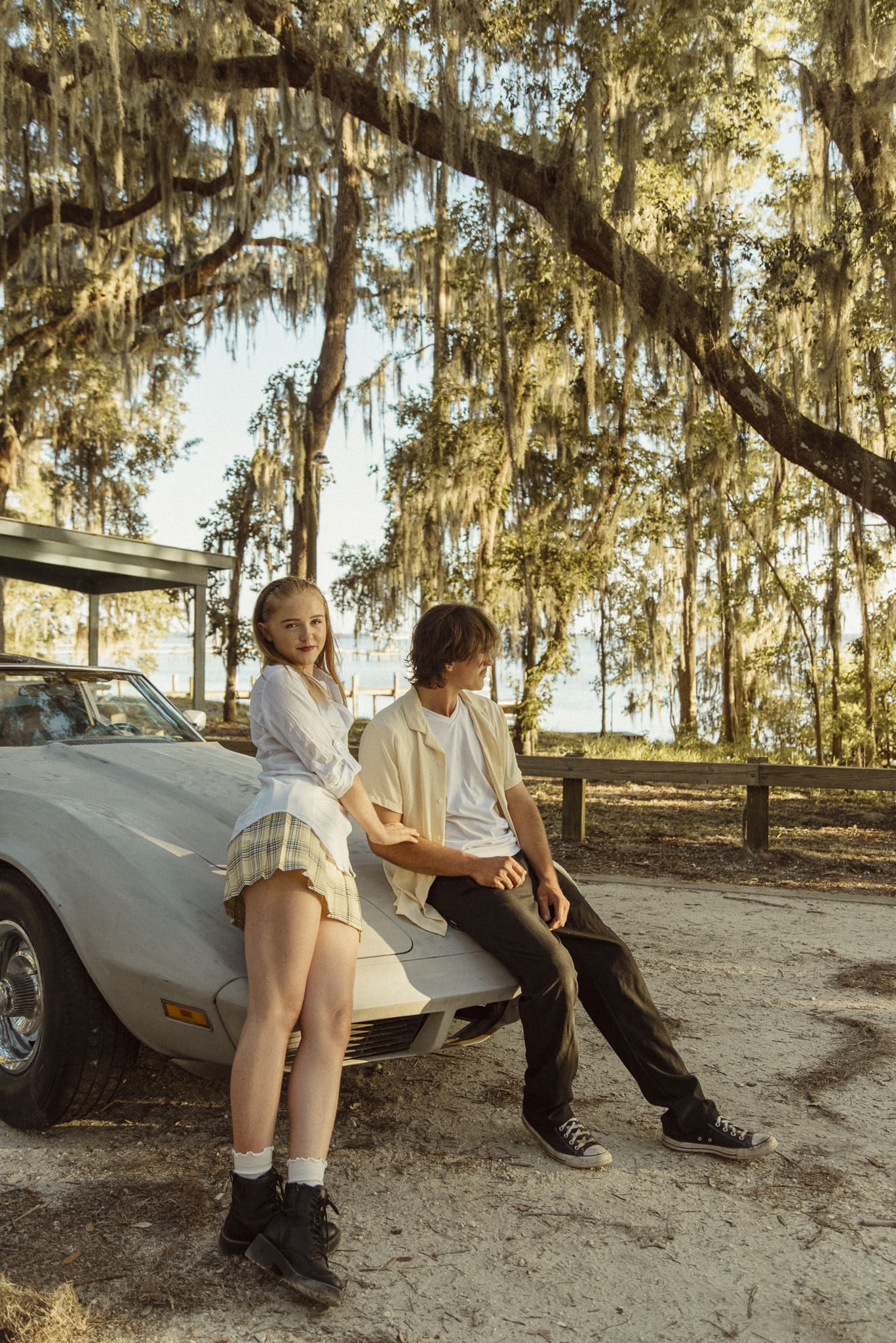 Editorial couples session featuring a couple sitting on a classic Corvette with golden light filtering through oak tress along the St. Johns River.