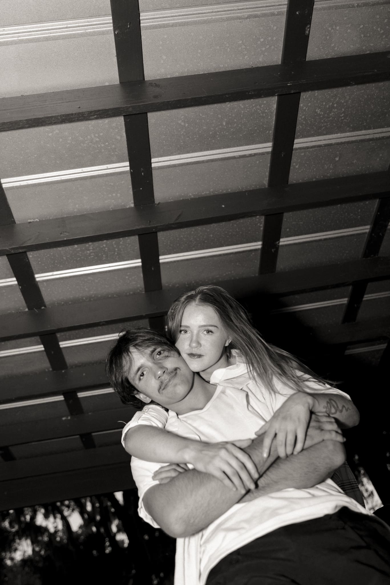 Black and white editorial couples portrait of a couple embracing under a pavilion, photographed from a low angle. 