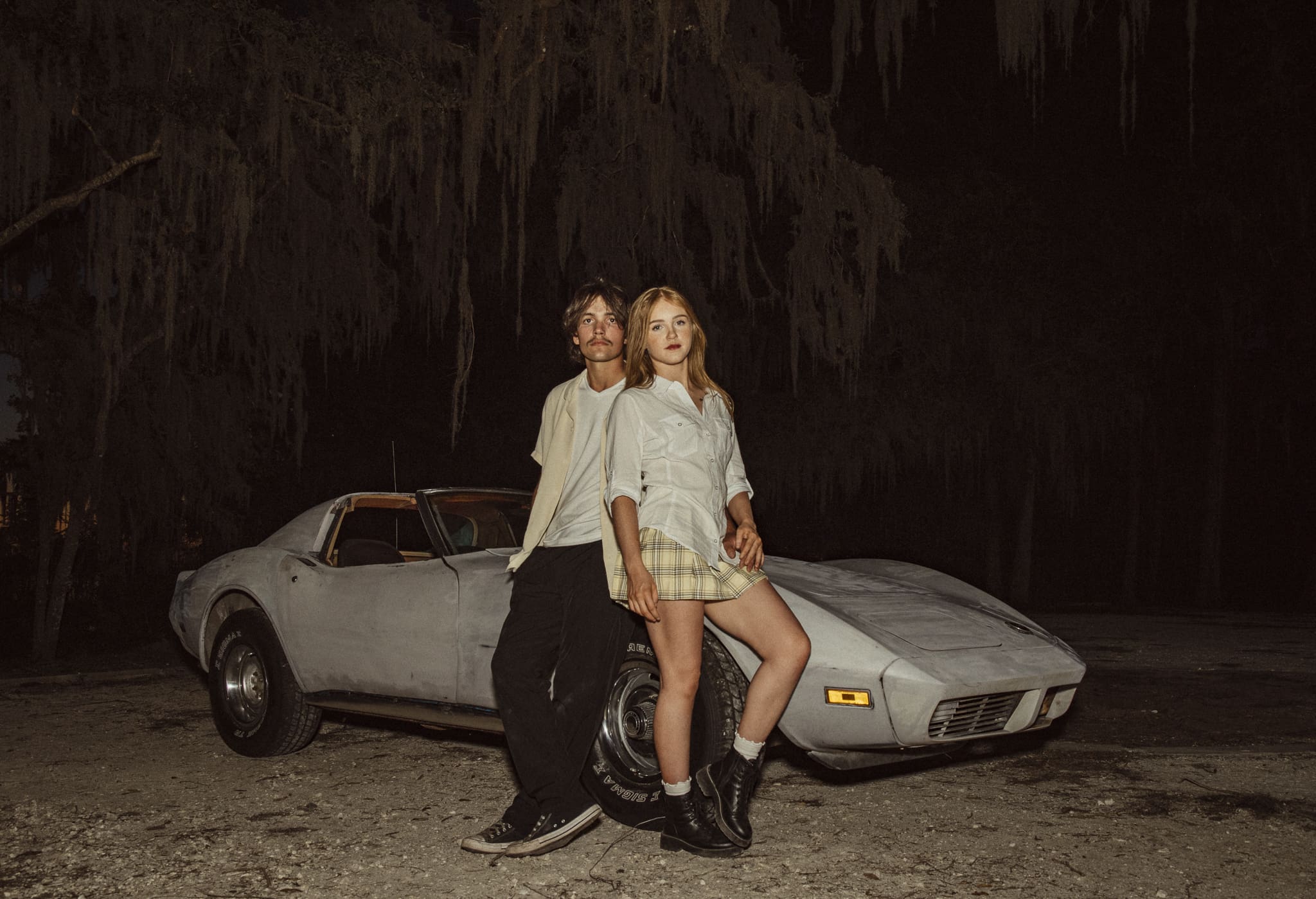 Editorial nighttime couples portrait of a couple standing confidently in front of a vintage Corvette, styled with flash photography. 