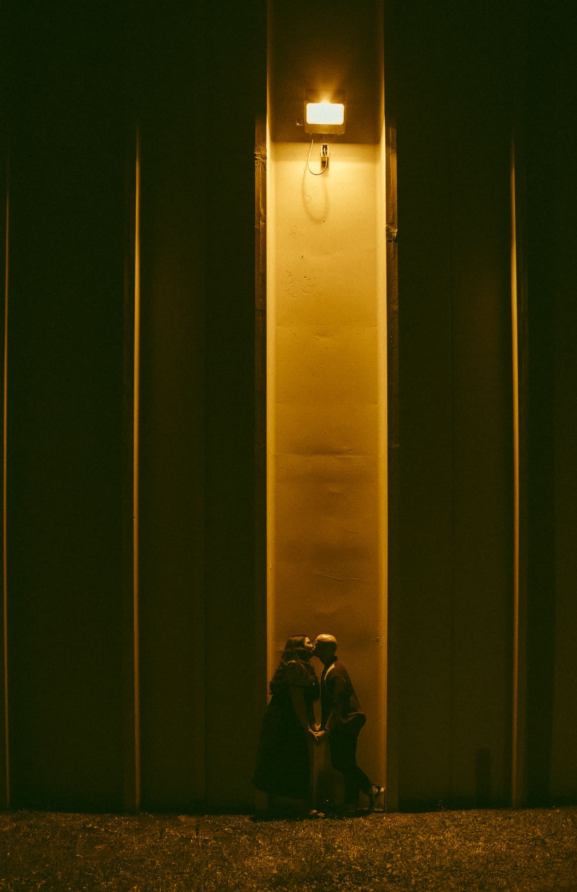 Rebecca and Noah kissing under warm yellow lighting during a nightime downtown St. Augustine engagement session with cinematic, editorial composition.