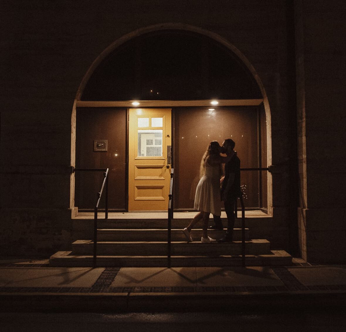 Editorial date night engagement session in St. Augustine featuring a couple kissing under a softly lit archway at night.