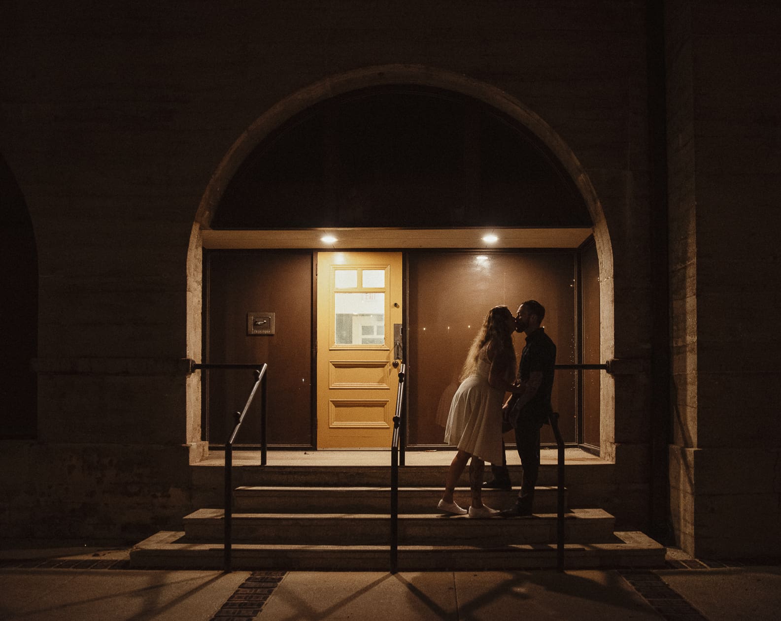 Bride and groom kissing beneath a softly lit arched doorway in historic downtown St. Augustine at night. 