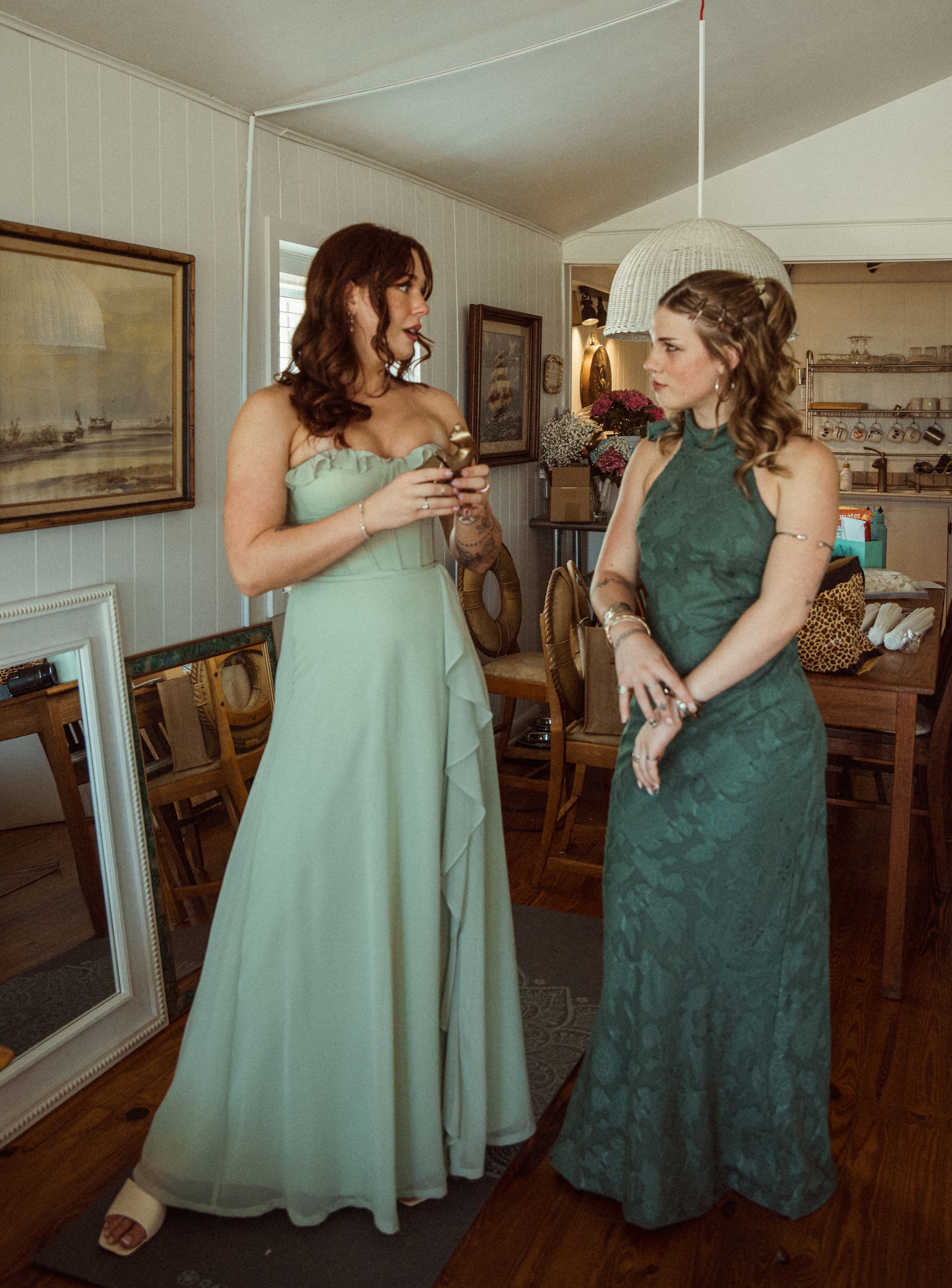 wo bridesmaids in green dresses chat in a bright, calm room before the wedding