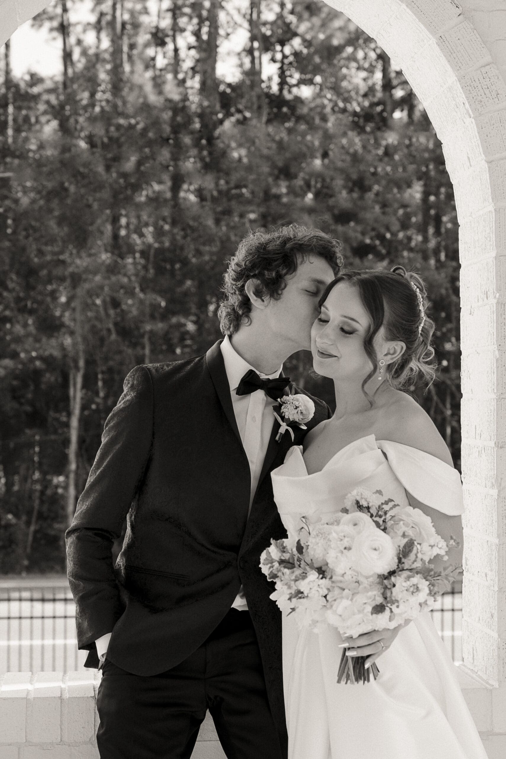Bride and groom standing together under an arch, eyes closed and calm, sharing a quiet moment before their wedding ceremony