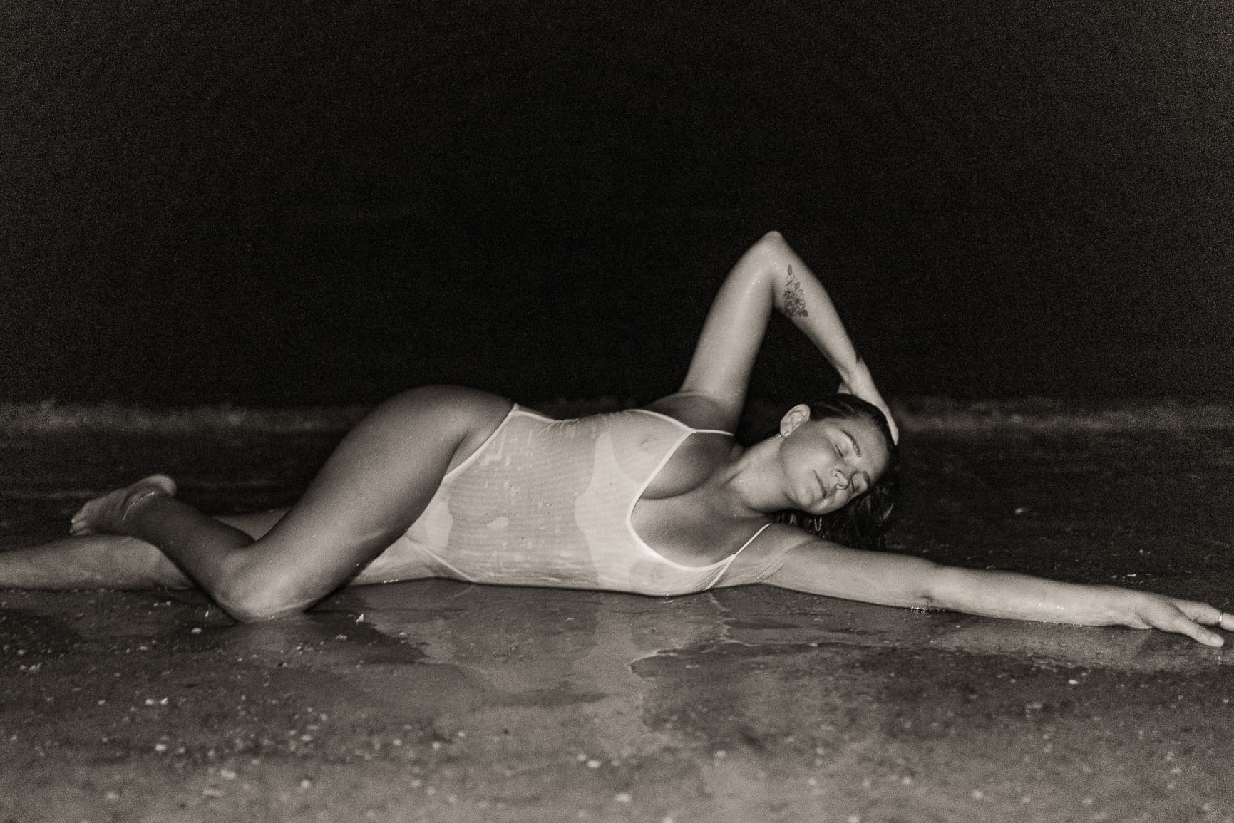 Woman reclining at the shoreline during an embodiment session, captured in an expressive pose that reflects emotional release and self-trust
