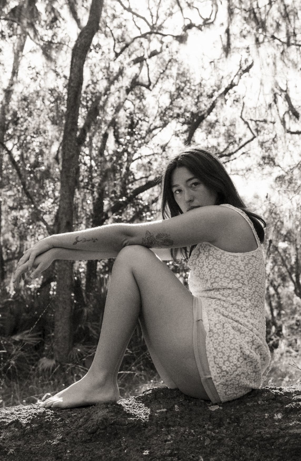 Woman seated outdoors in a quiet, natural setting during an embodiment photography session, appearing grounded, present, and deeply connected to self