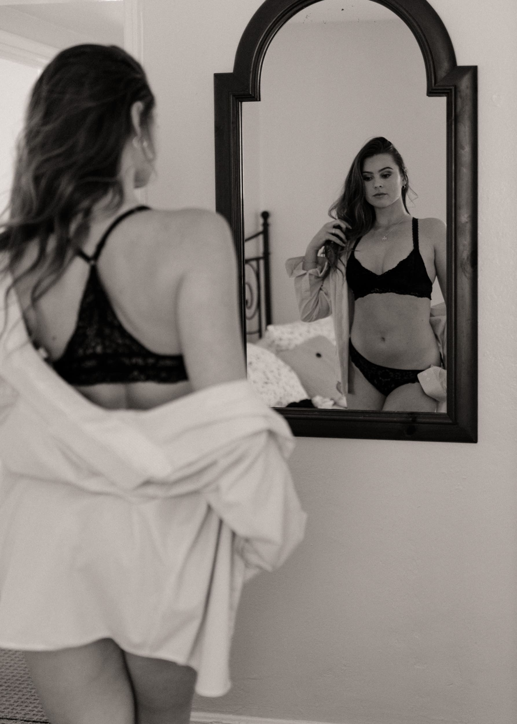 Woman standing in front of a mirror during an embodiment photography session, calmly observing herself with presence and self-trust