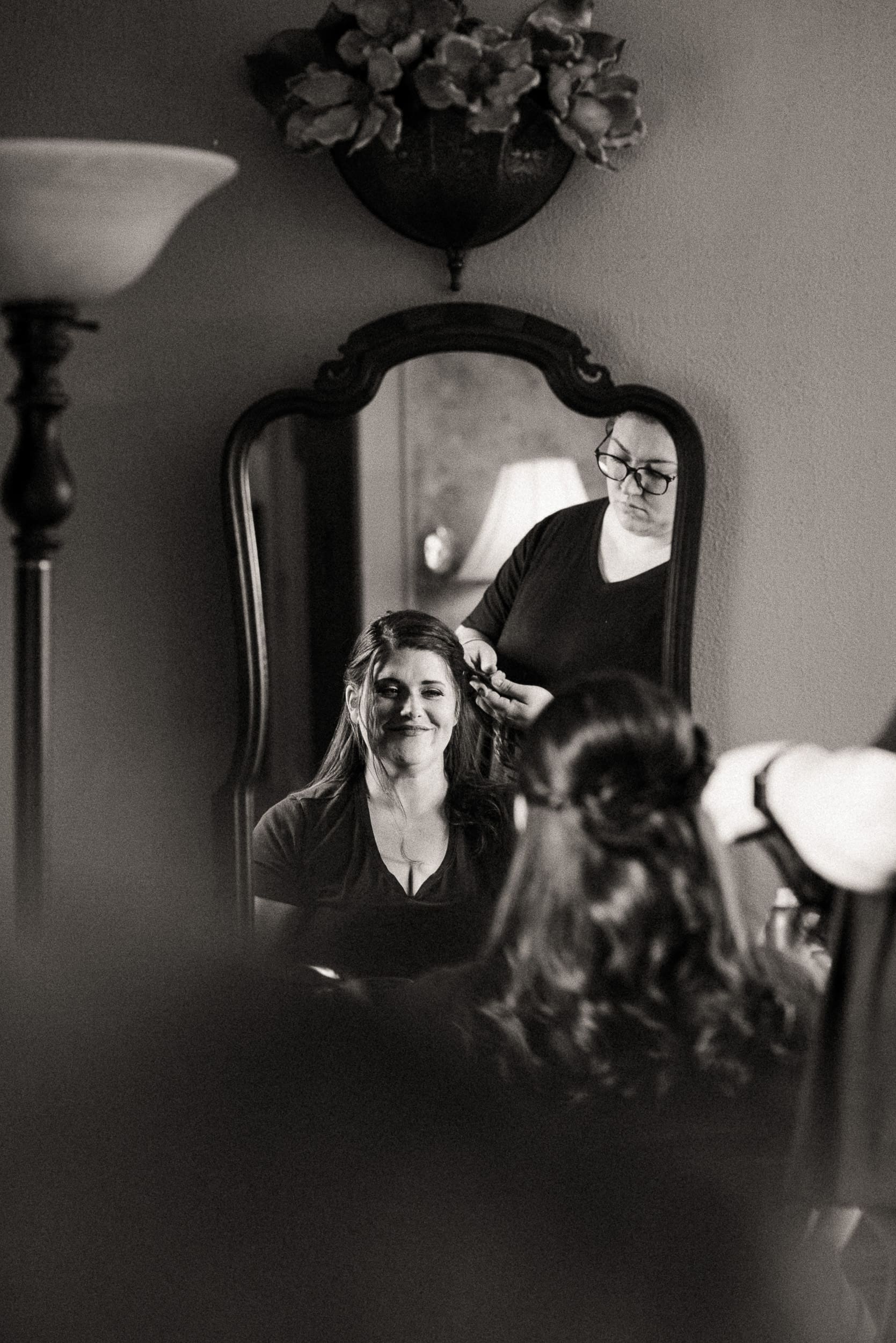 Bride sitting calmly while having her hair styled during wedding morning preparations, appearing supported and relaxed before the ceremony