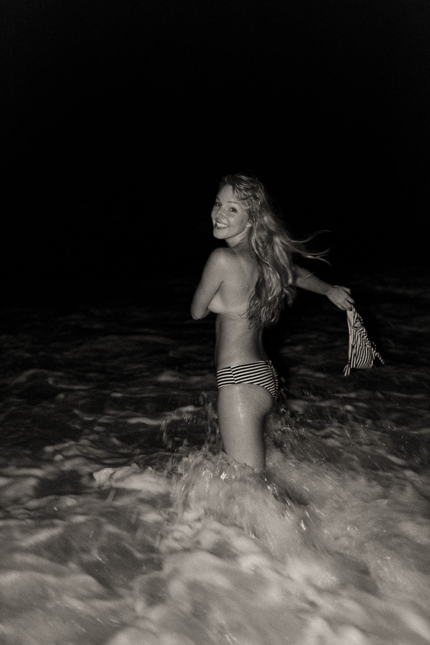 Woman standing in the ocean at night during an embodiment photography session, arms open and hair moving in the wind, expressing freedom, presence, and embodied self-connection.