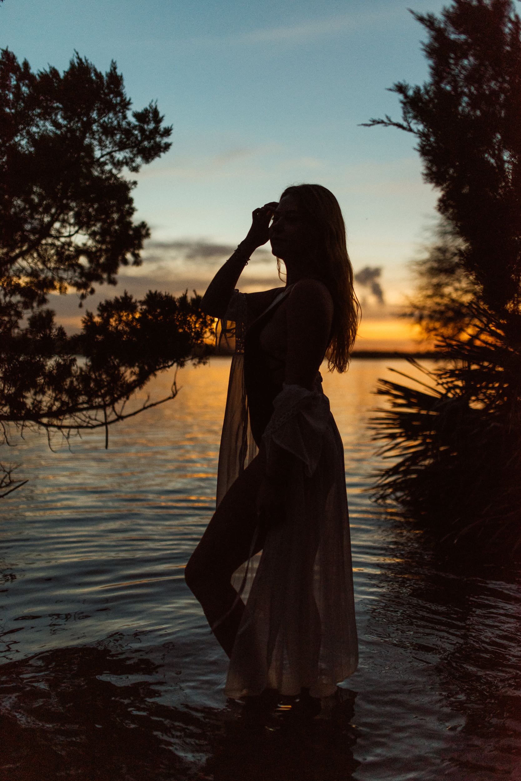 Woman silhouetted at sunset by the water during an embodiment photography session, expressing presence, self-connection, and embodied feminine energy