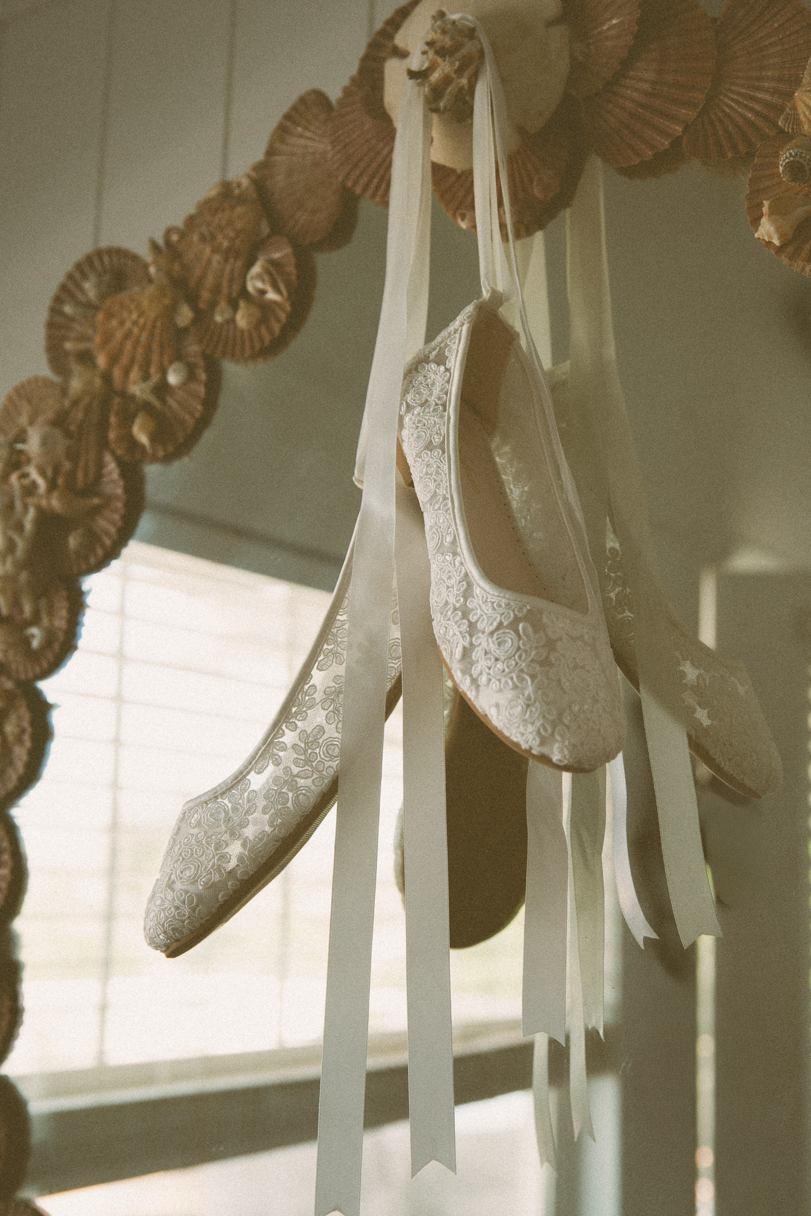 Embroidered lace bridal flats hanging by ivory ribbons beside a gold pleated fan garland