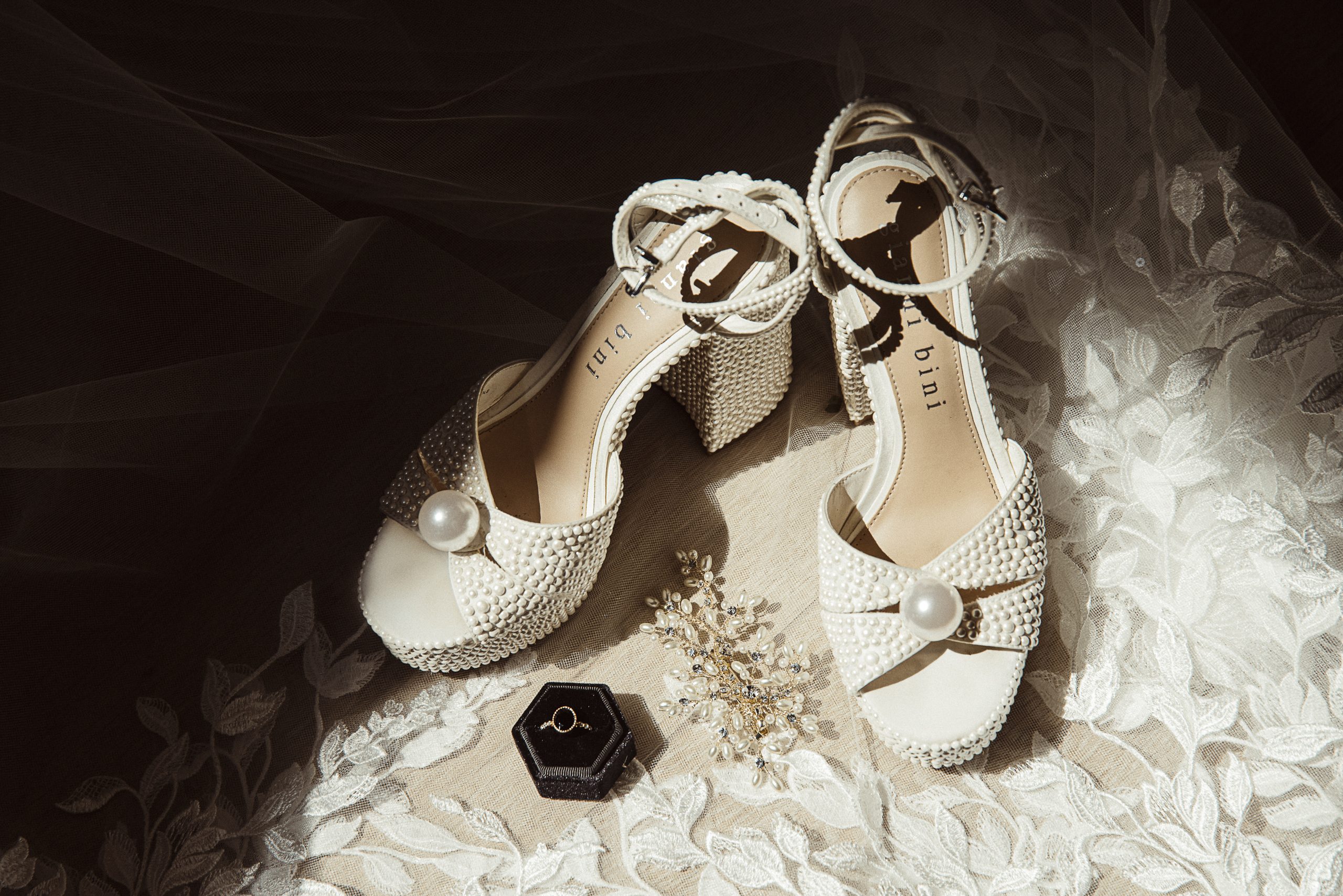 Pearl-covered bridal heels styled with a black velvet ring box and pearl hair vine on lace