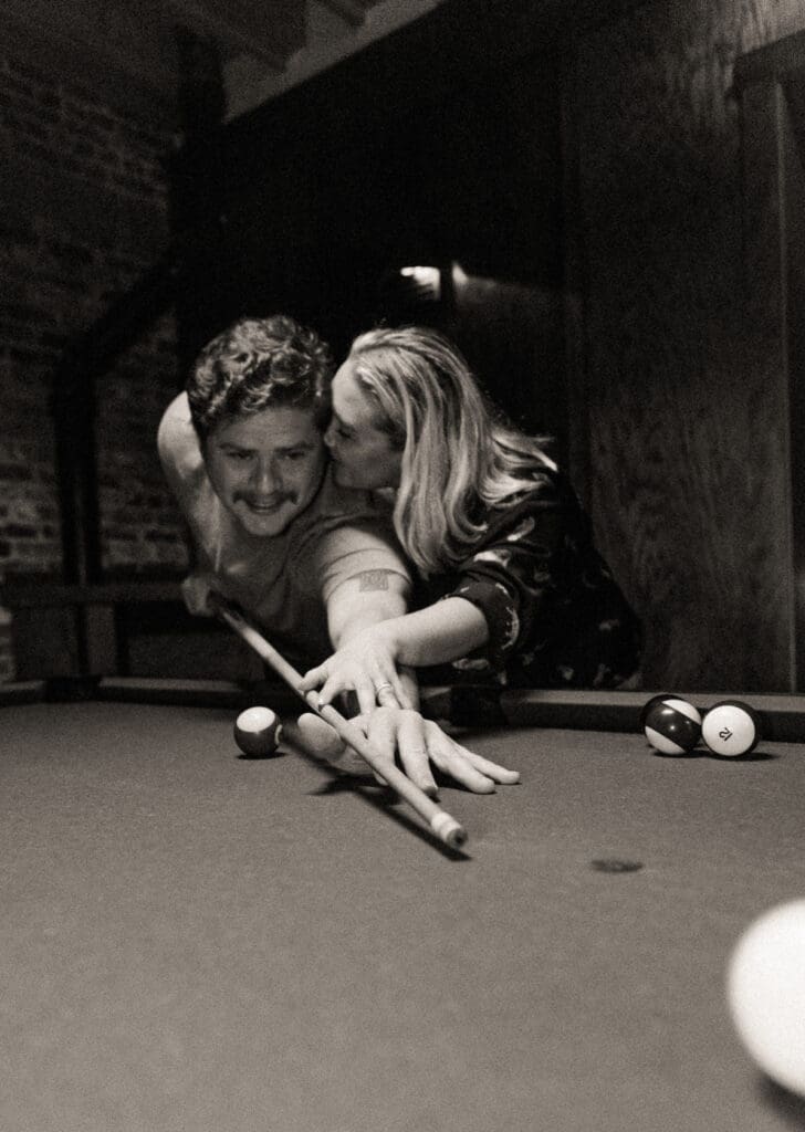 Playful couple playing pool together during a nighttime engagement shoot at a local bar in St. Augustine, Florida. 