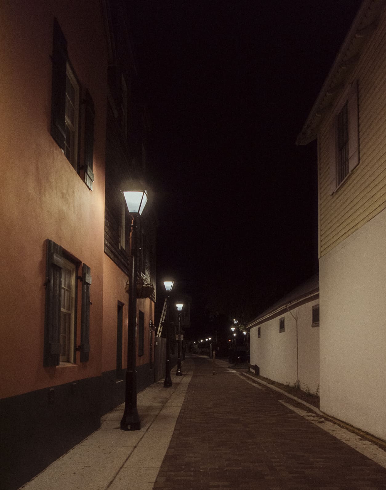 Quiet historic alley with colonial architecture and street lamps glowing in downtown St. Augustine at night.