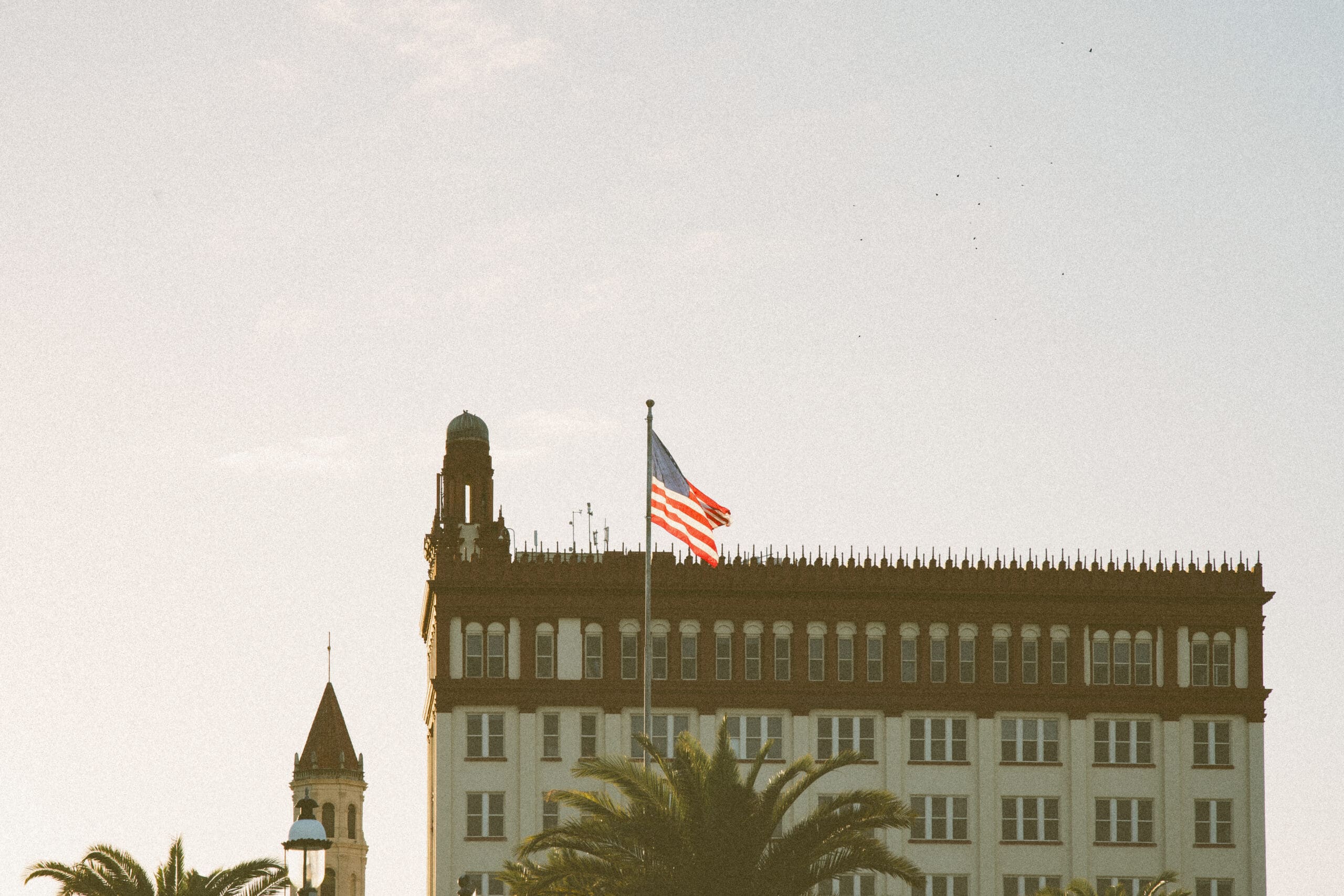 American flag flying above historic Spanish-style building in downtown St. Augustine at sunset. 