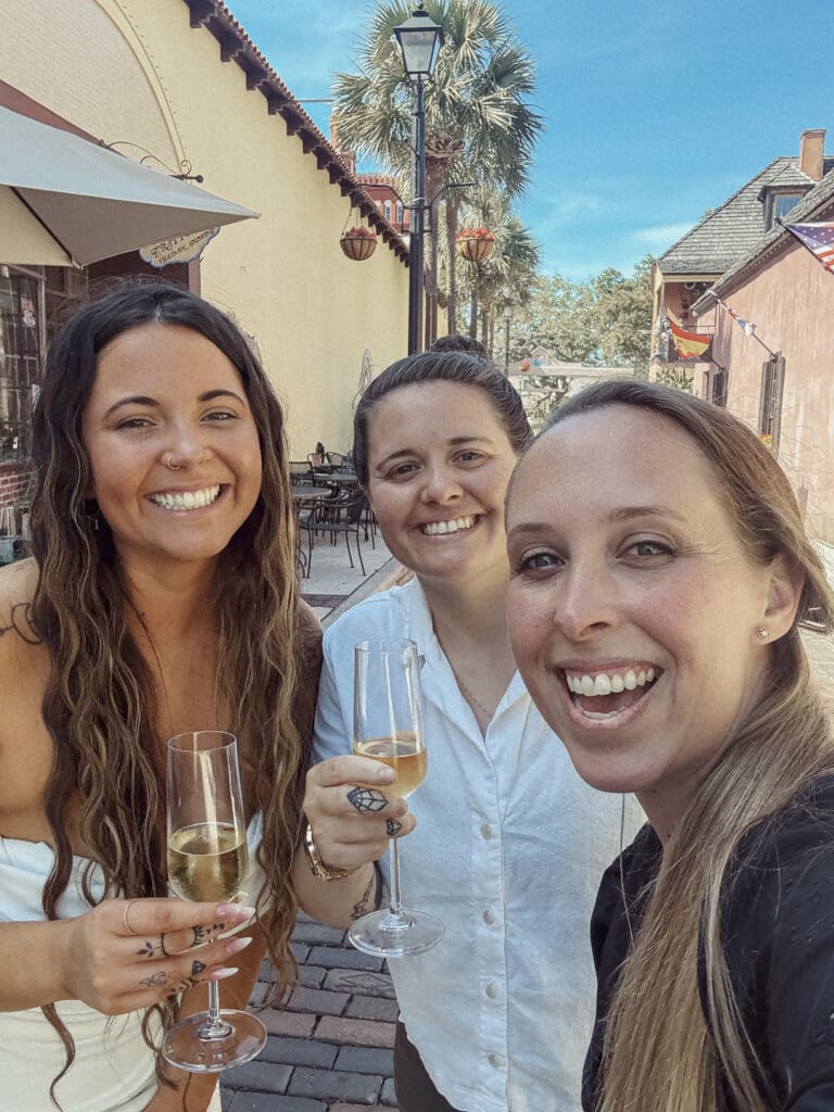 Friends enjoying champagne together at a sunny outdoor restaurant in St. Augustine during a wedding weekend brunch. 