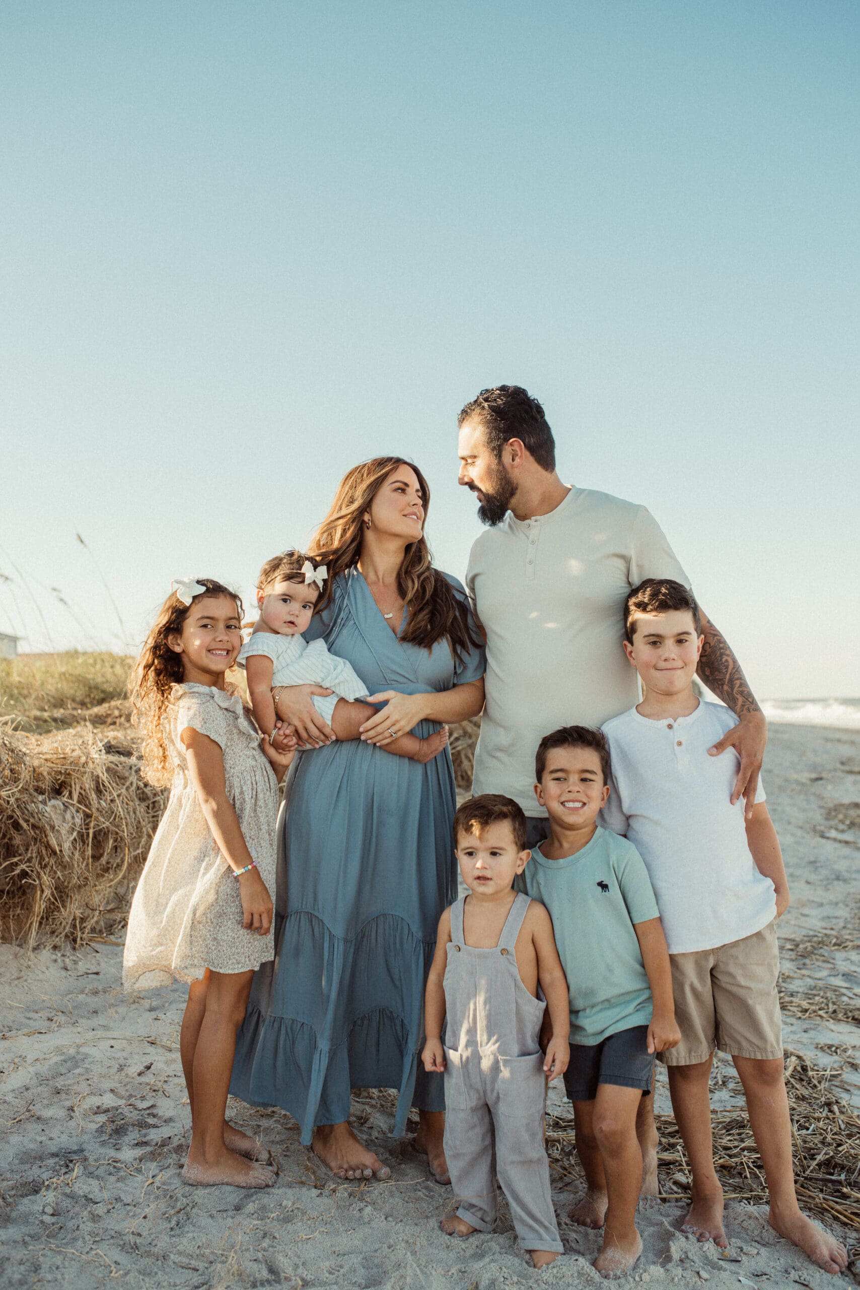 Large family wearing soft neutral and blue tones during sunset beach family photo session.