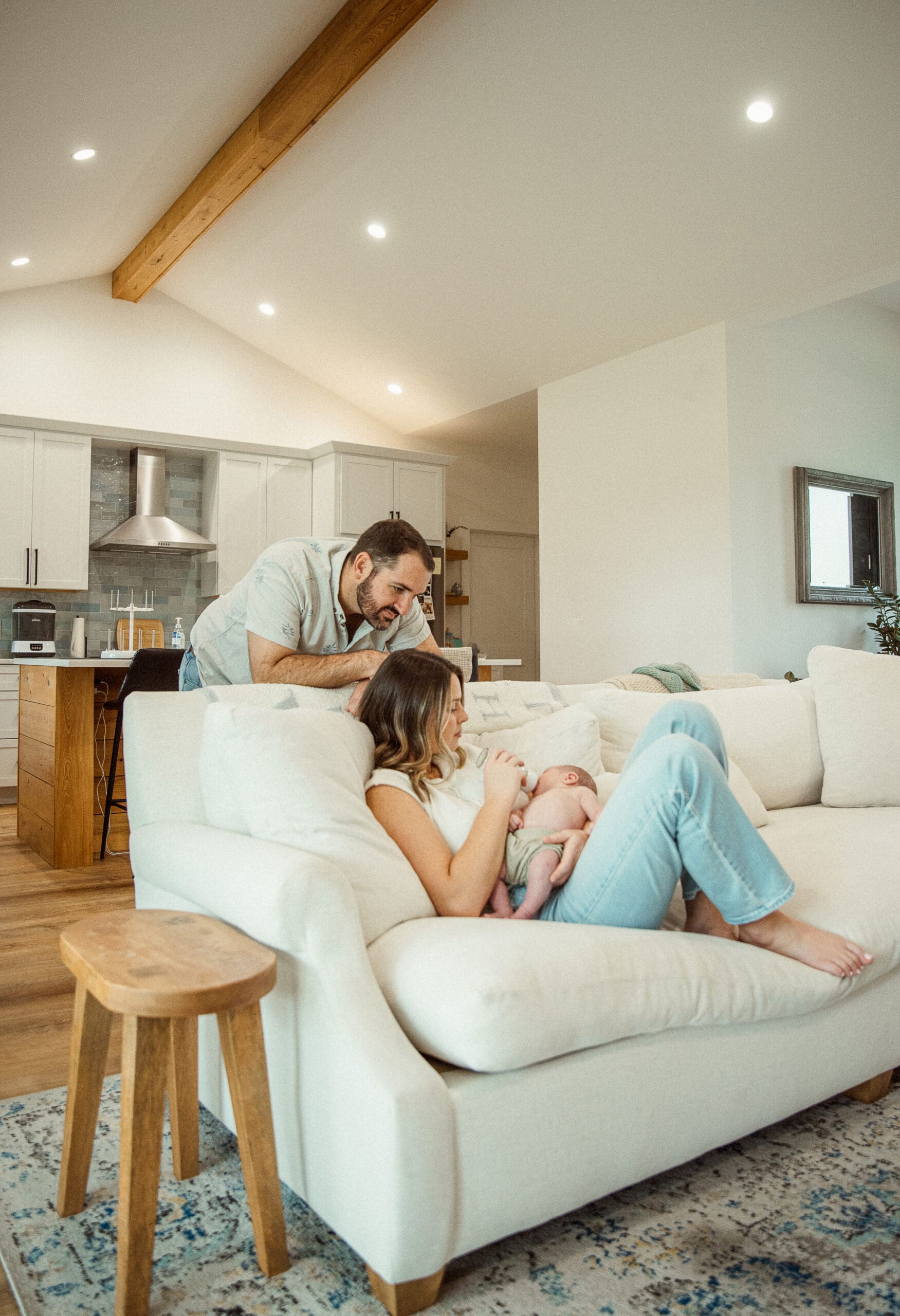 In-home family photo session with neutral tones and soft textures on a couch with parents and newborn.