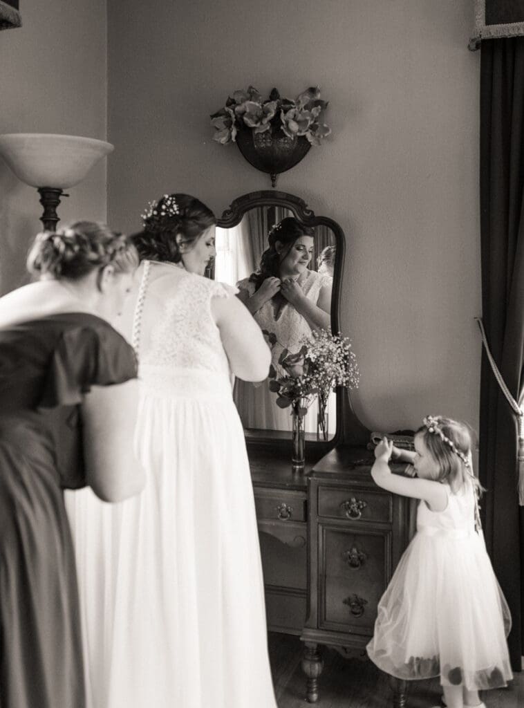 Bride adjusting her dress in mirror during quiet black and white getting ready moment. 