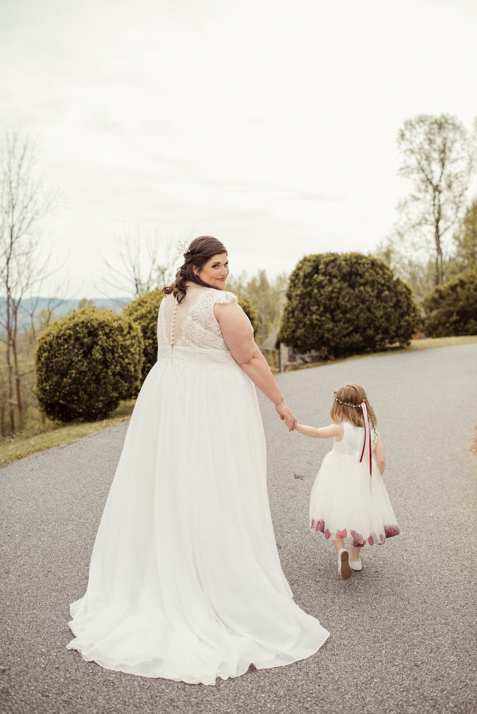 Bride holding her daughter's hand while walking together after ceremony in mountain setting. 