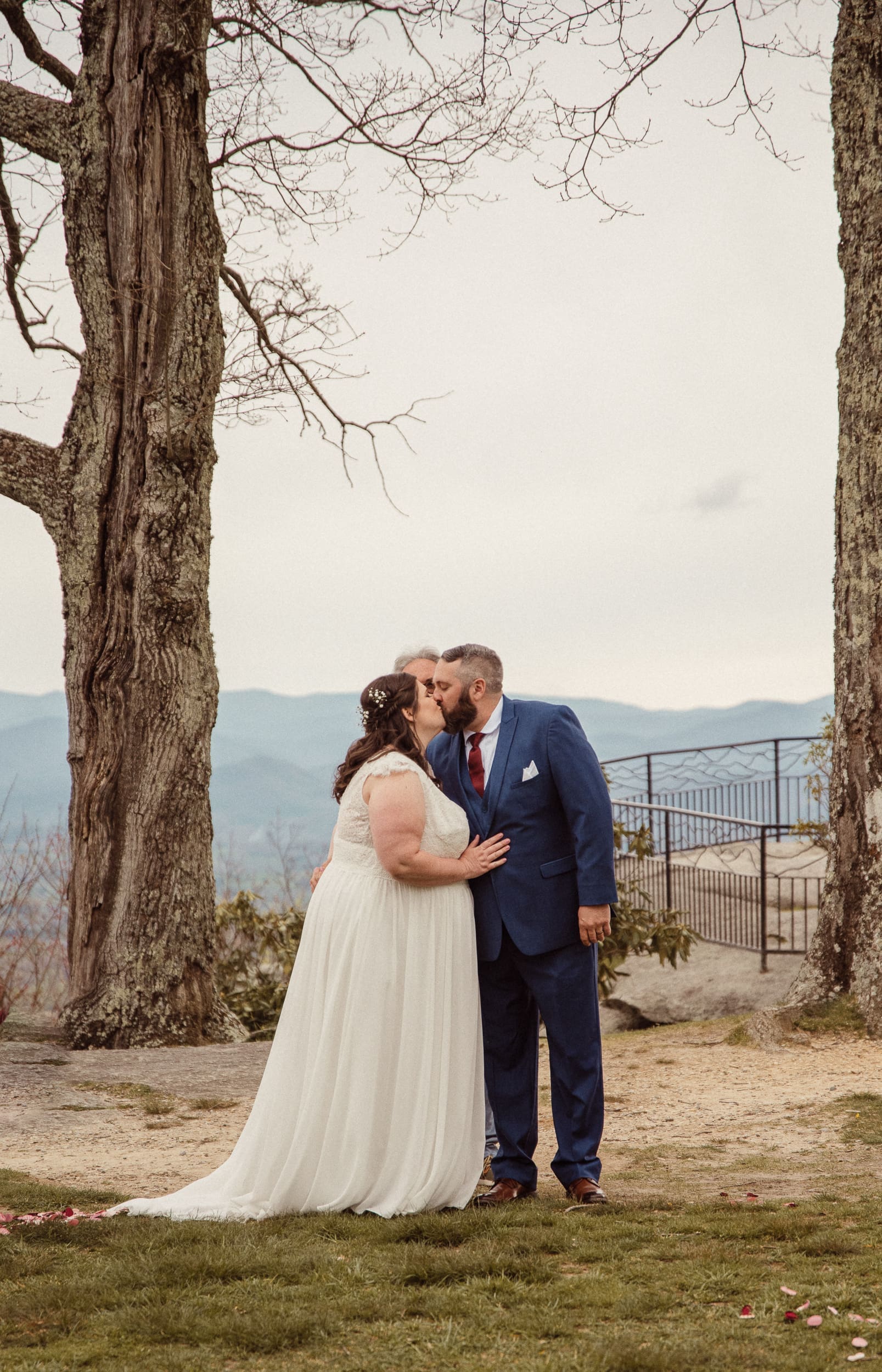 Bride and groom sharing first kiss during mountain wedding ceremony with scenic overlook