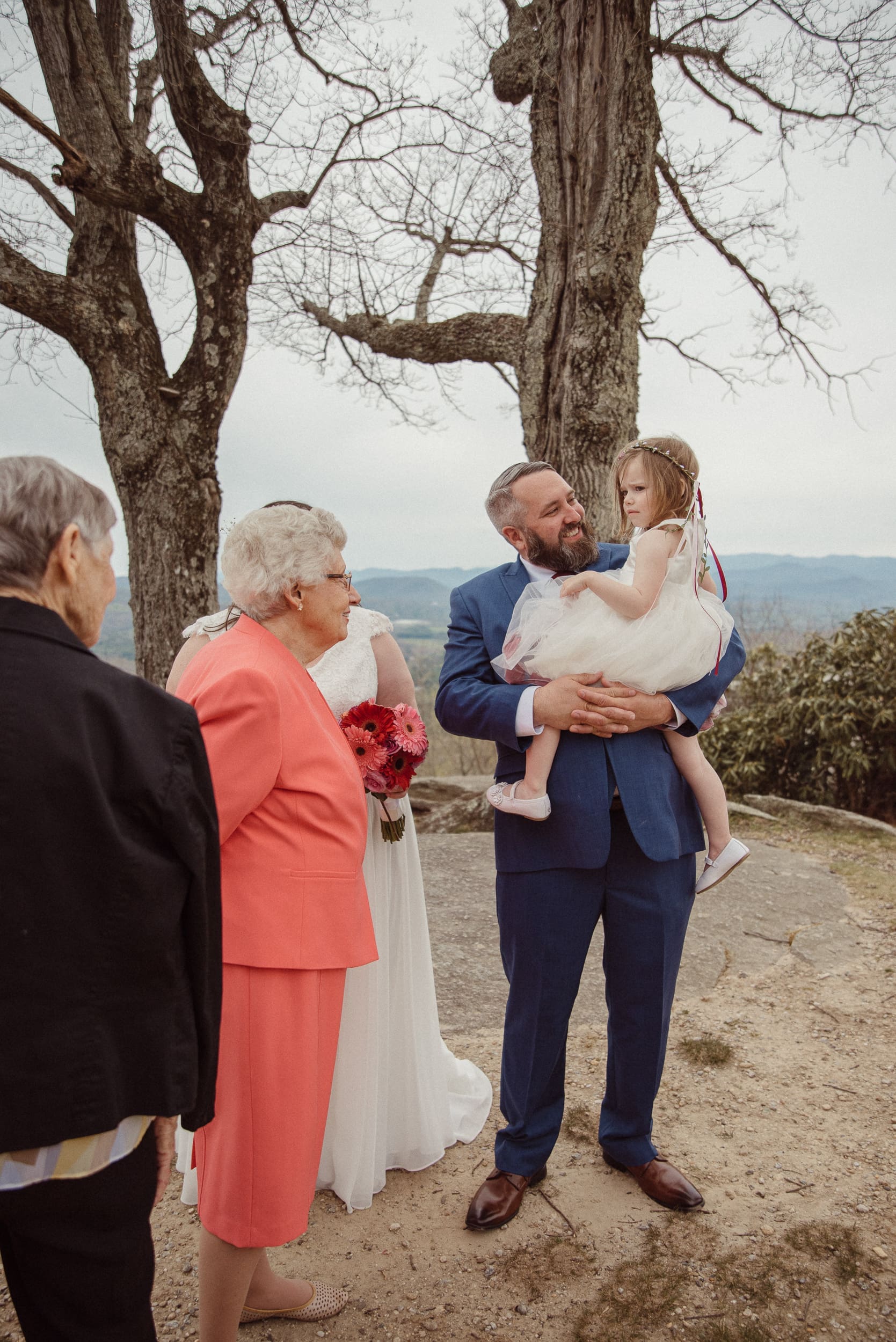 Groom holding child during candid family moment after mountain wedding ceremony