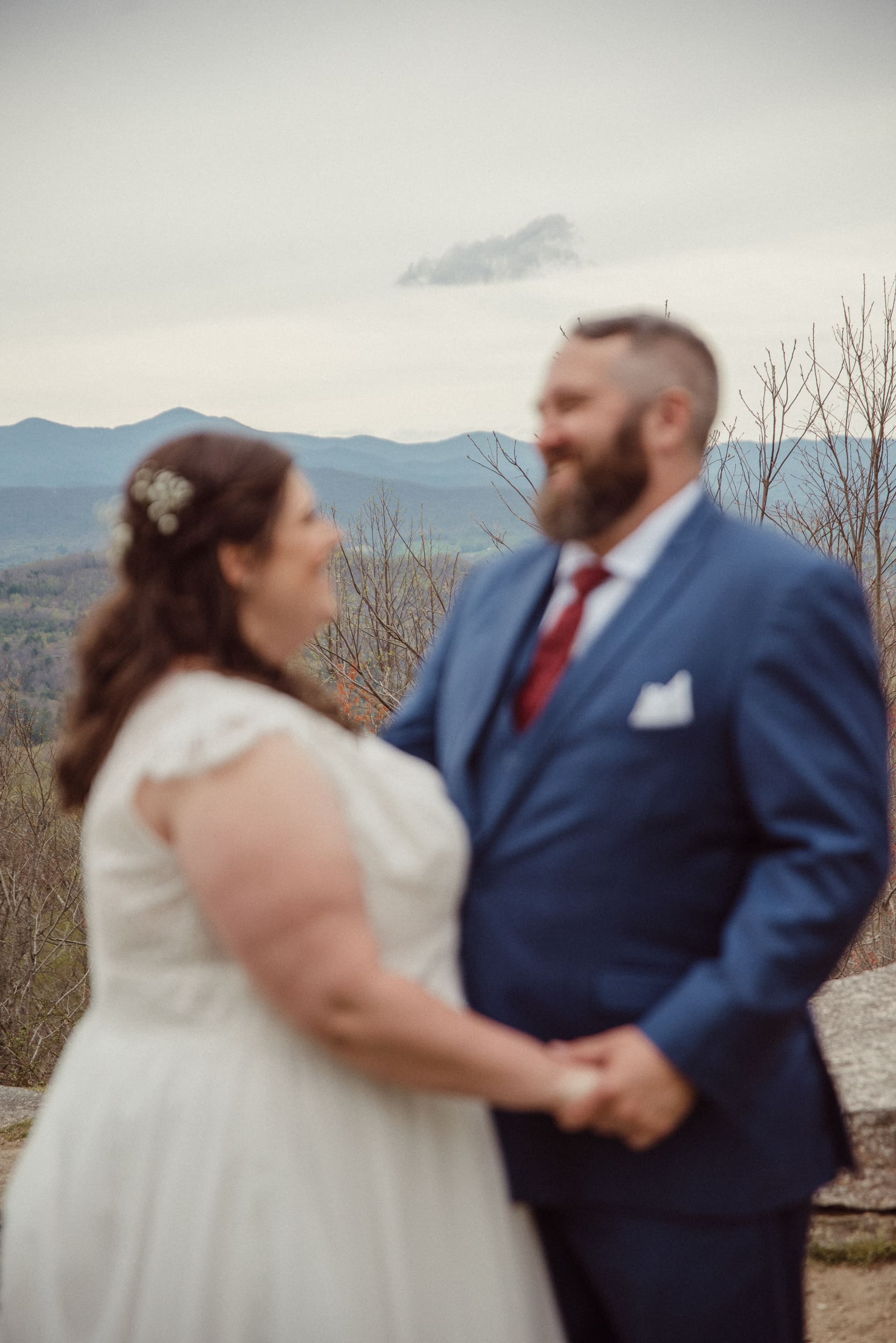 Bride and groom holding hands with soft mountain views during intimate Blue Ridge wedding portraits. 